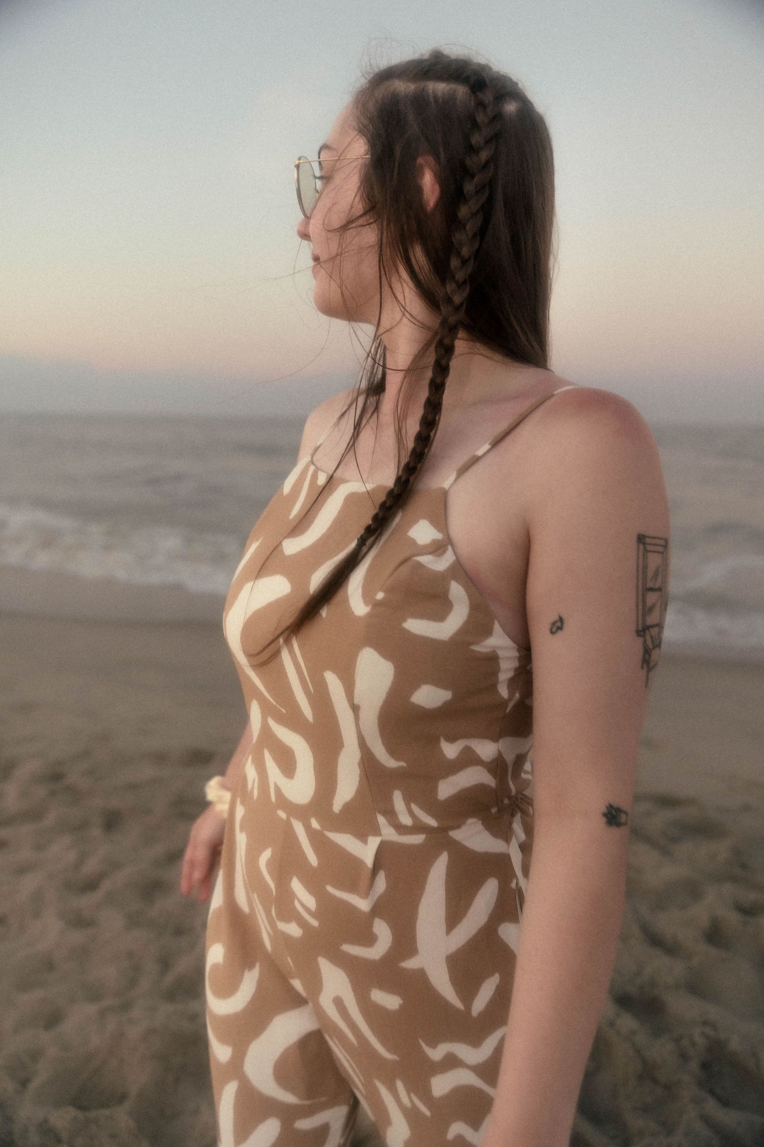 Side profile of someone with braided hair wearing a tan patterned dress on the beach.