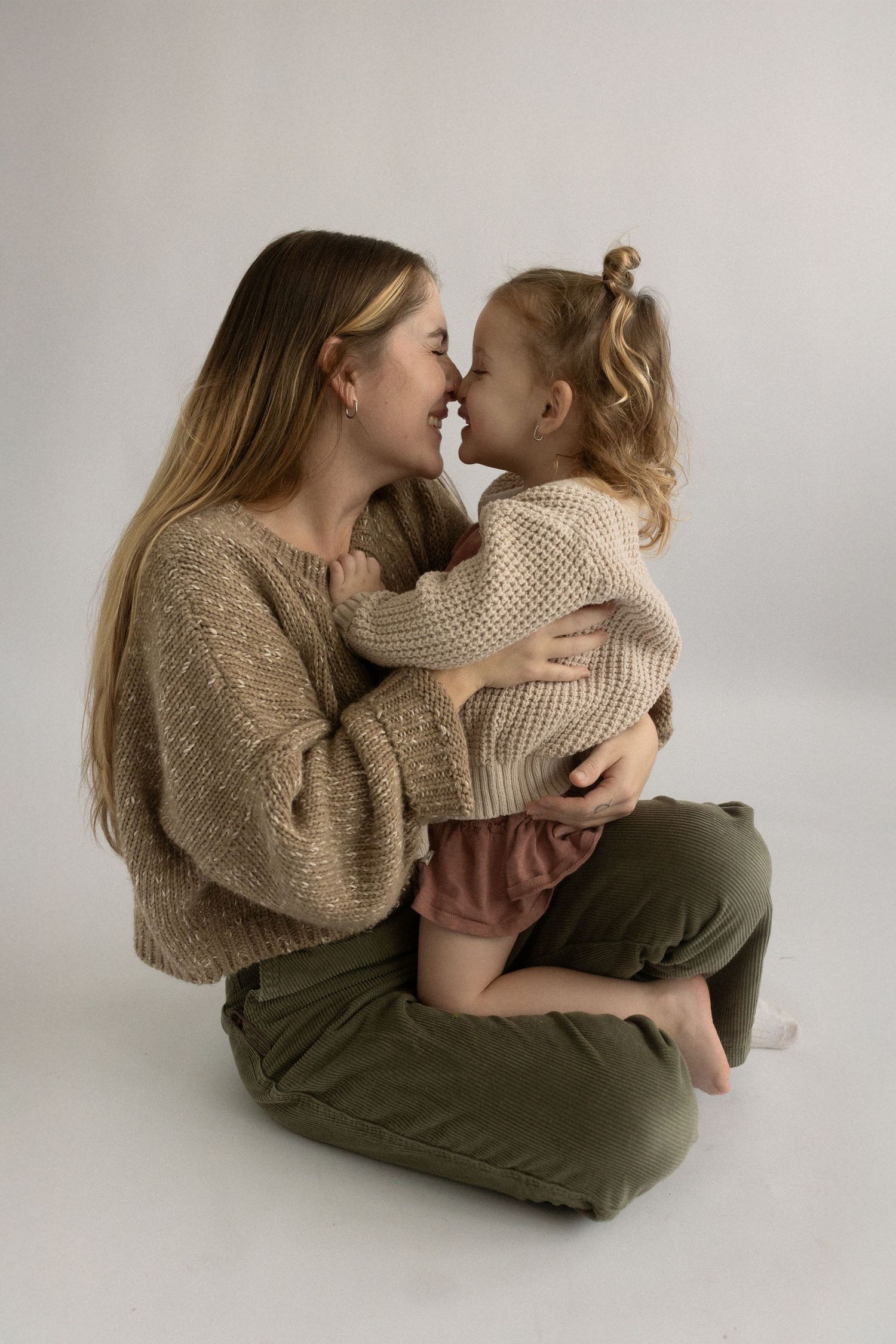 Joyful candid moment between parent and child wearing cozy sweaters in studio setting.