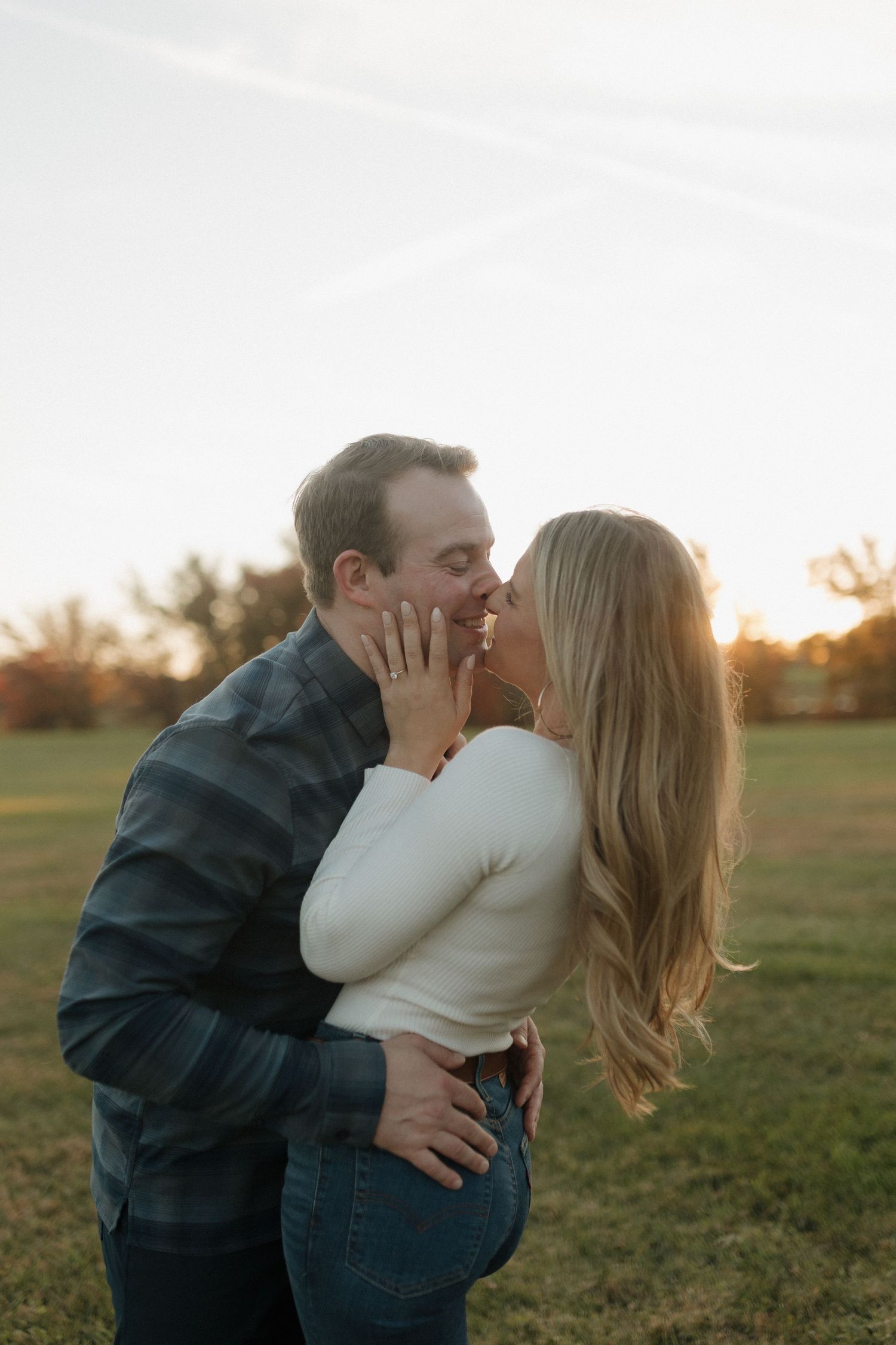 Couple sharing romantic kiss together in field during golden hour sunset.