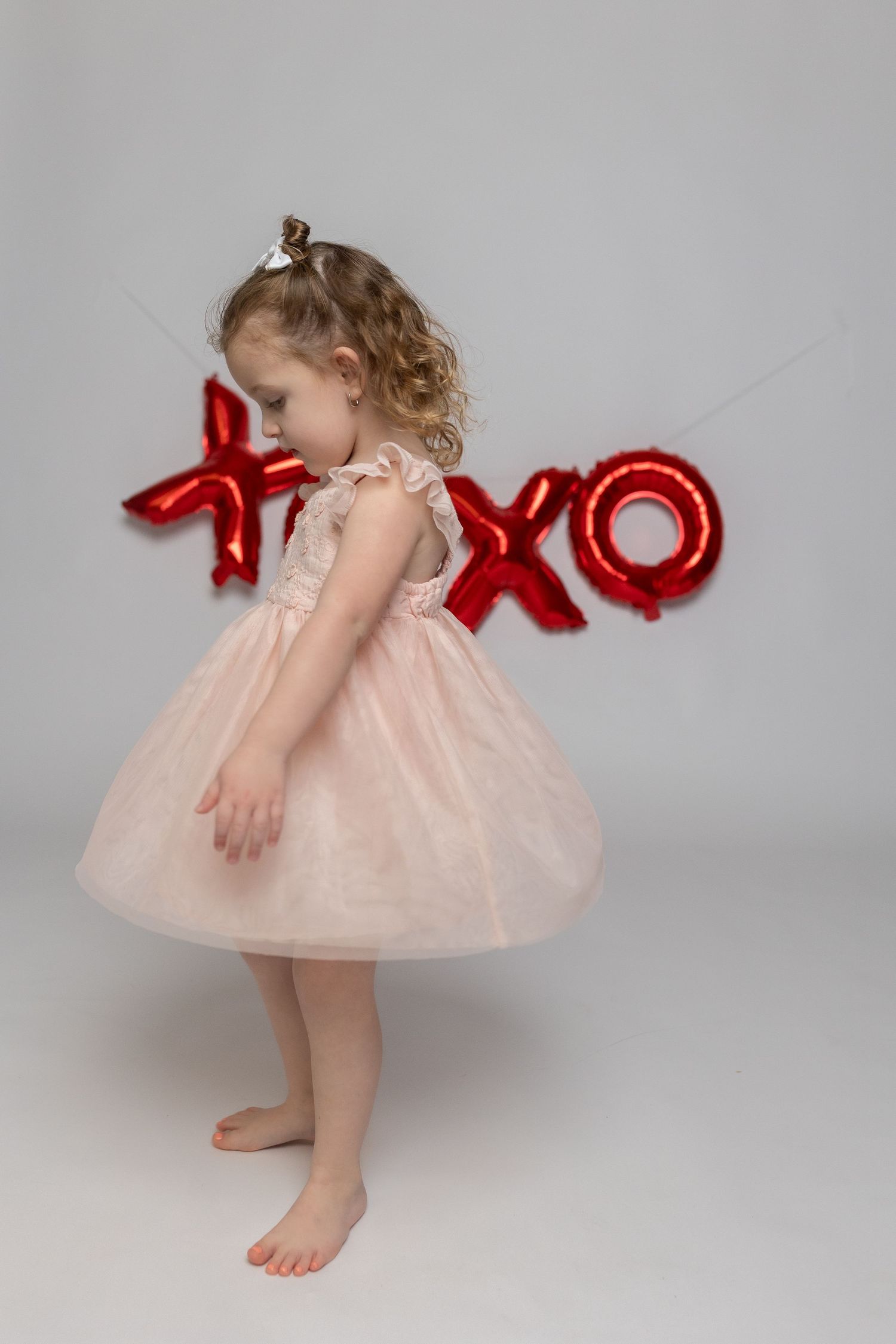 A child in a pink tulle dress posing in front of red XOXO balloon letters.