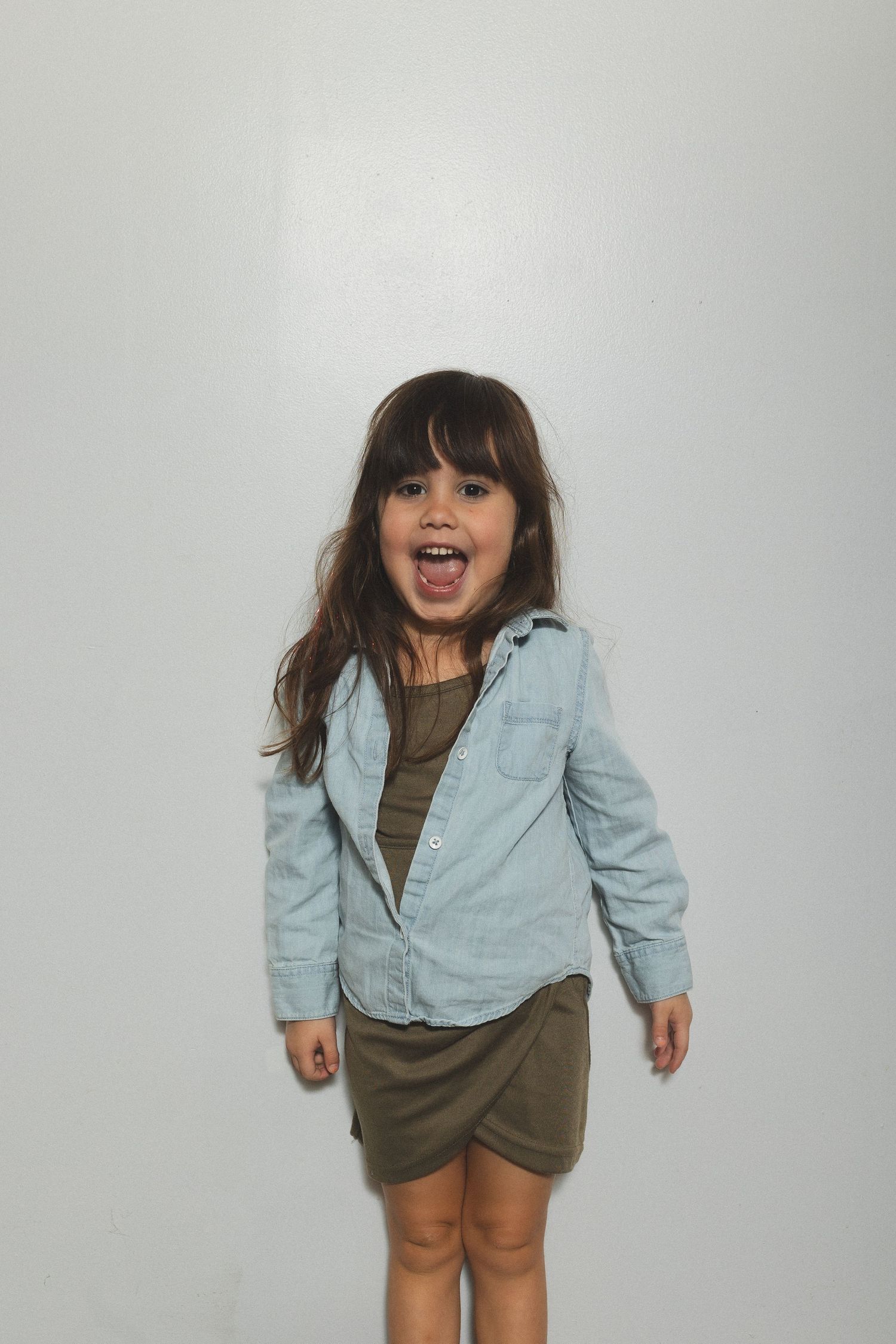 Young child in denim jacket making excited expression against white background.