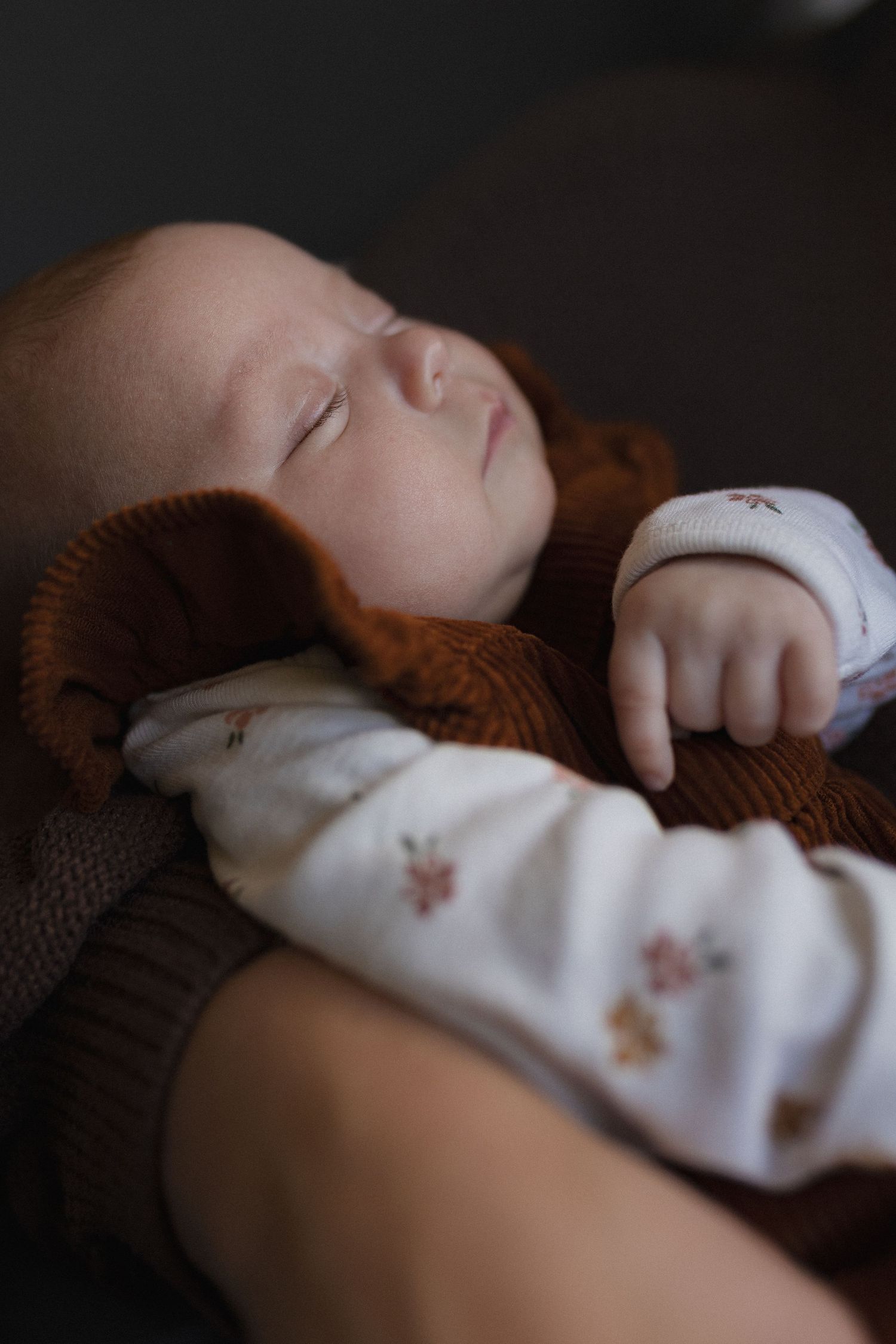 A sleeping infant in white clothing with brown accents rests peacefully.