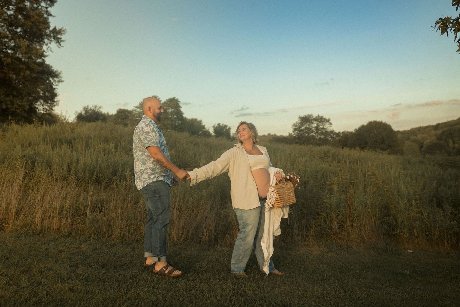 Couple holding hands in field during golden hour sunset.