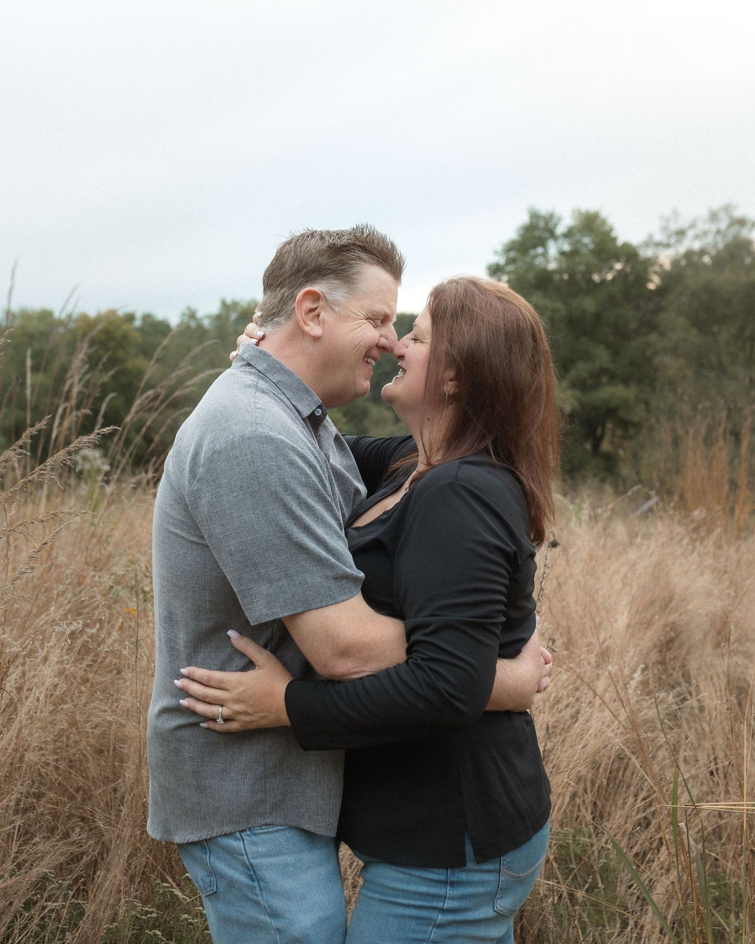A couple embraces romantically in a field of tall brown grass during an autumn photoshoot.