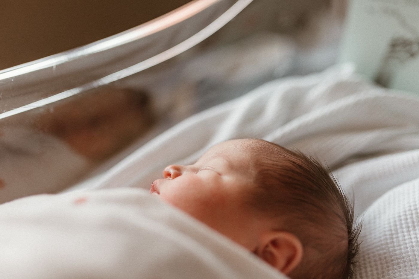 Side profile of newborn resting in hospital bassinet during fresh 48, wrapped in dotted swaddle, shot in warm tones and soft focus.