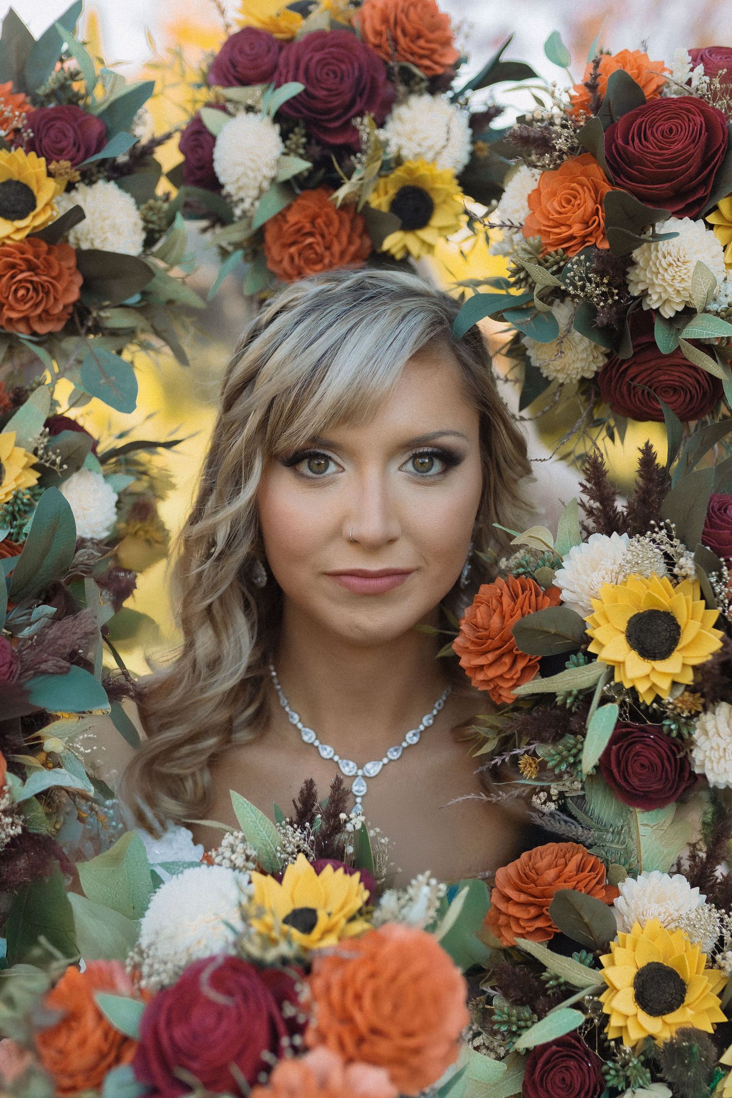 A bridal portrait framed by vibrant autumn flowers including sunflowers and deep red roses.
