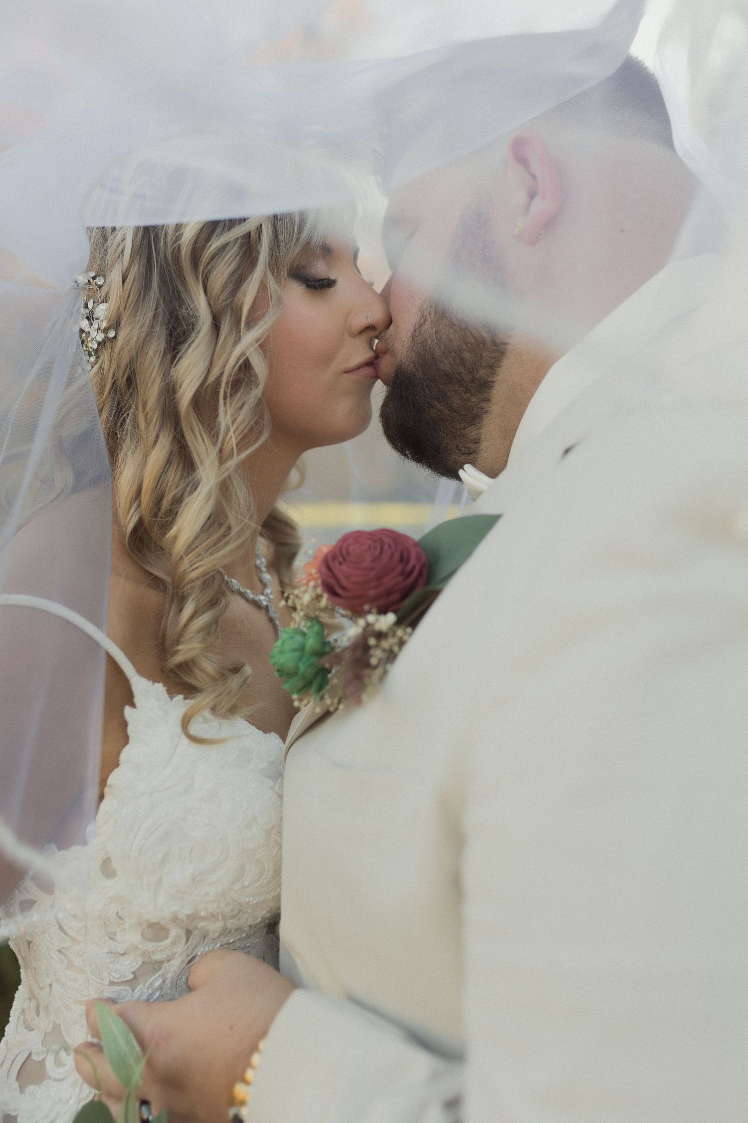 A romantic wedding portrait captured through a veil with a red rose bouquet.