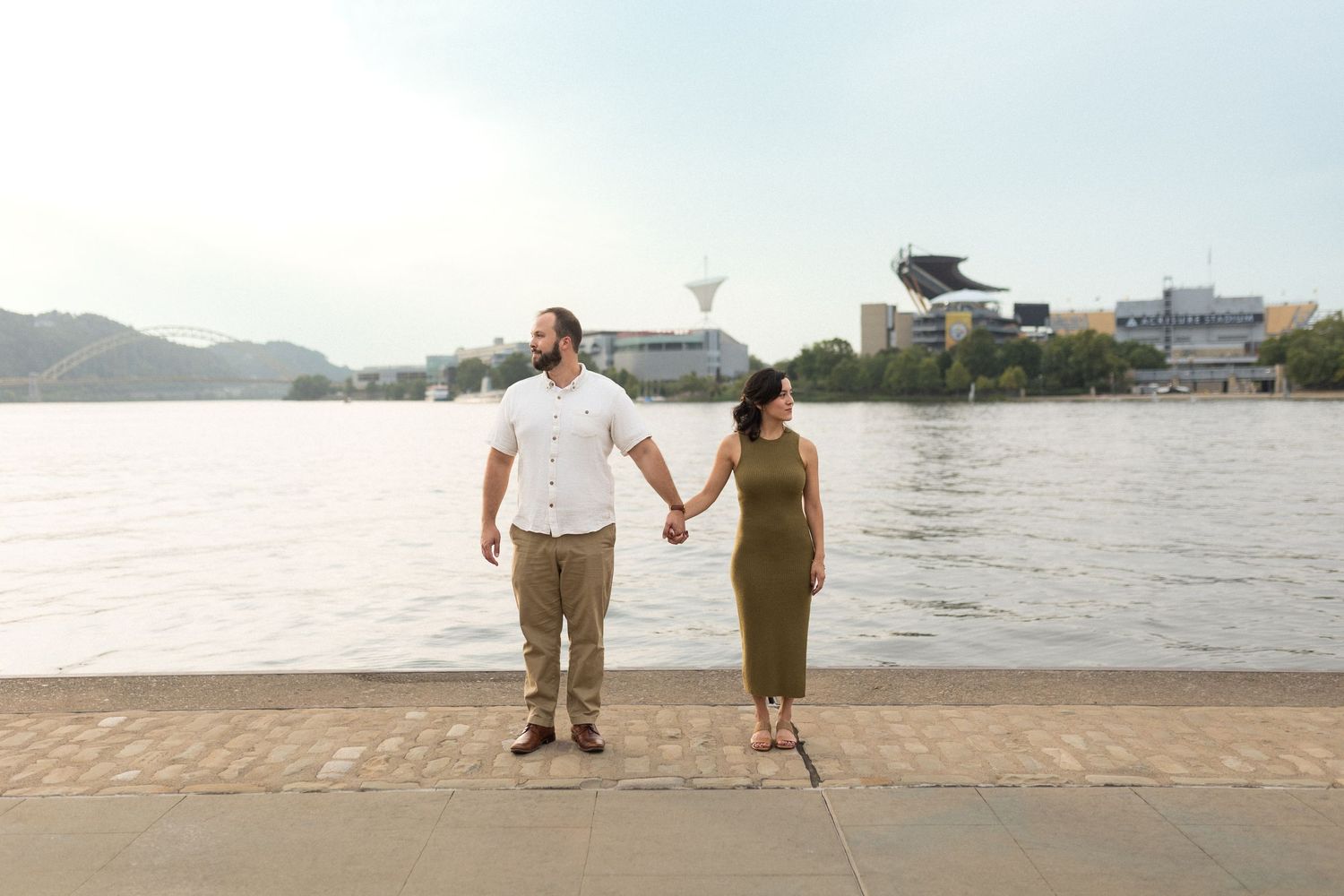 Couple holding hands while standing by river during sunset.