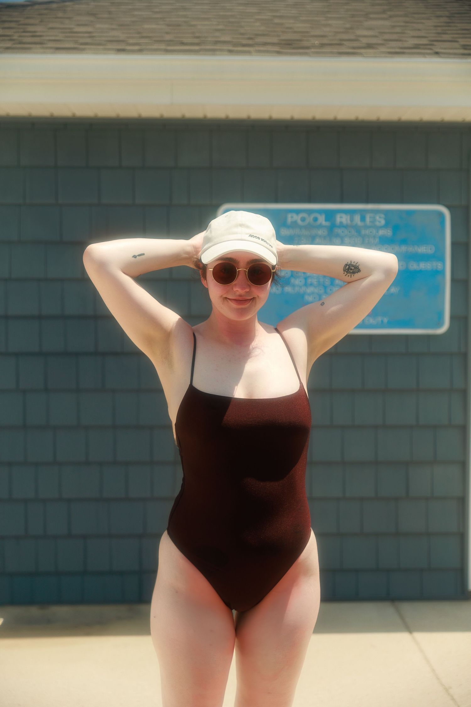 Summer pool scene with person in brown swimsuit and white hat.