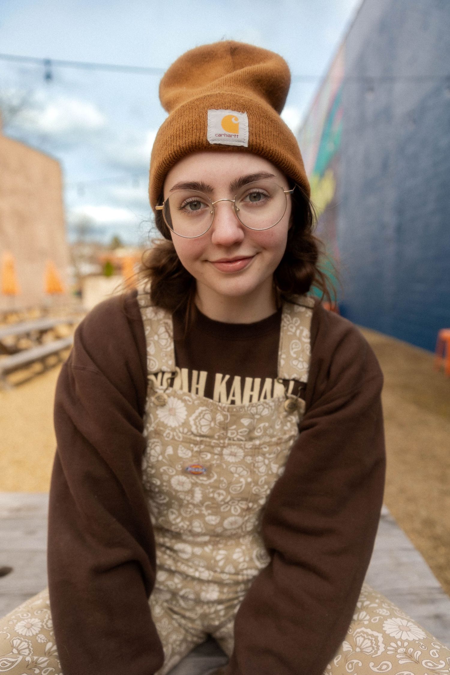 Cozy winter style with Carhartt beanie, glasses and patterned overalls in outdoor setting.