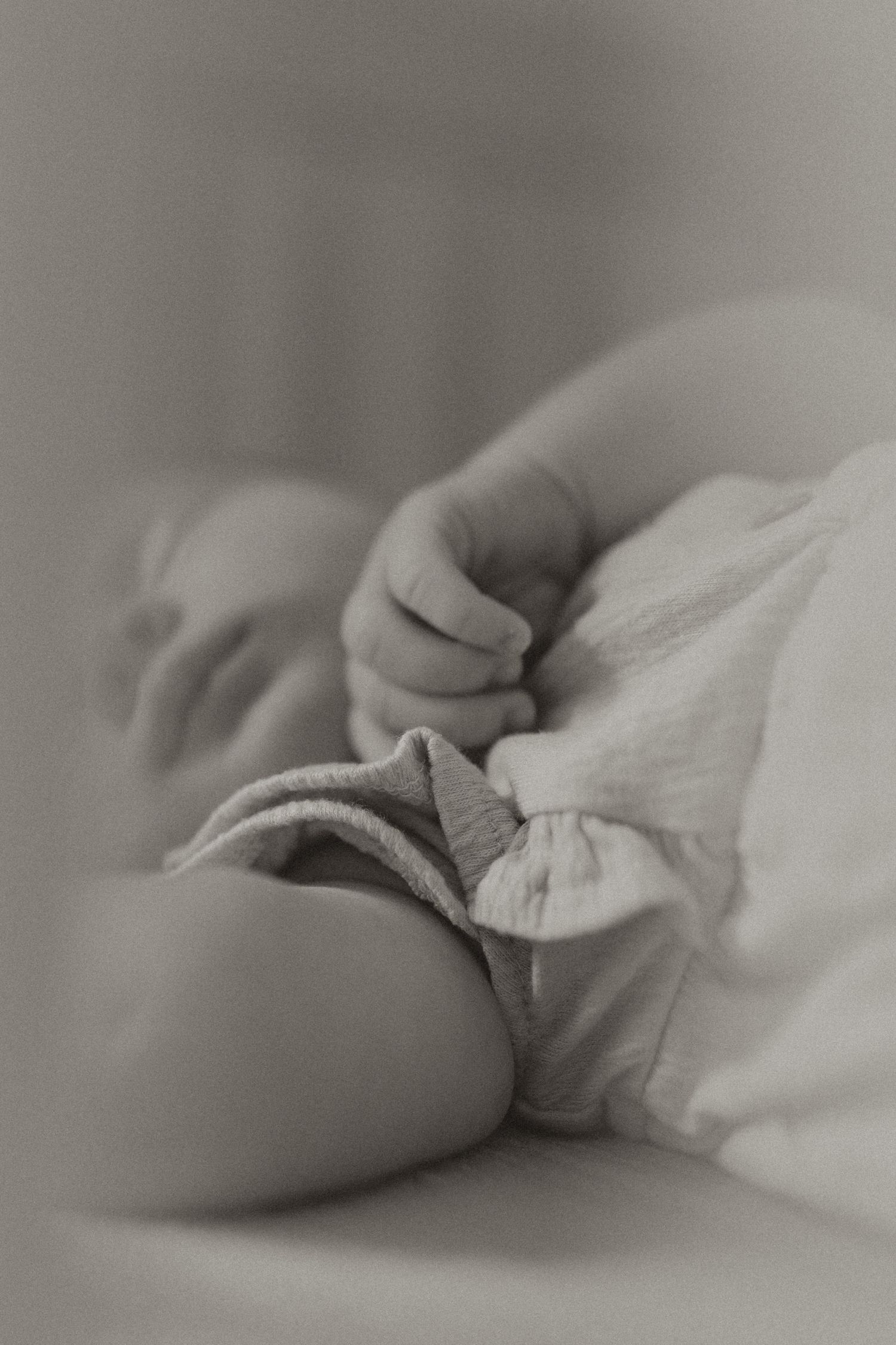 Artistic black and white close-up of infant's hand and clothing.