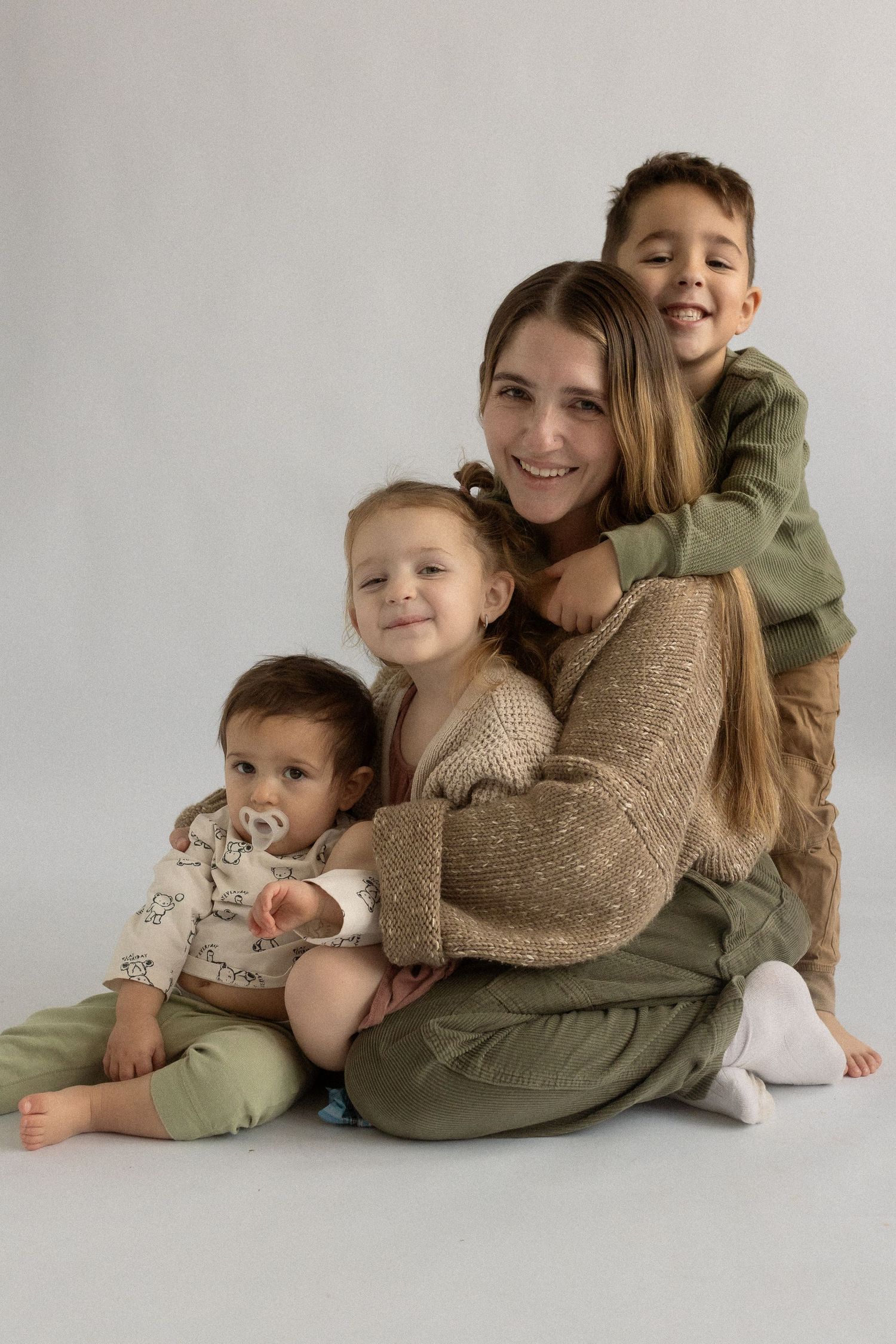 Studio portrait of parent and three children in cozy sweaters sitting close together.