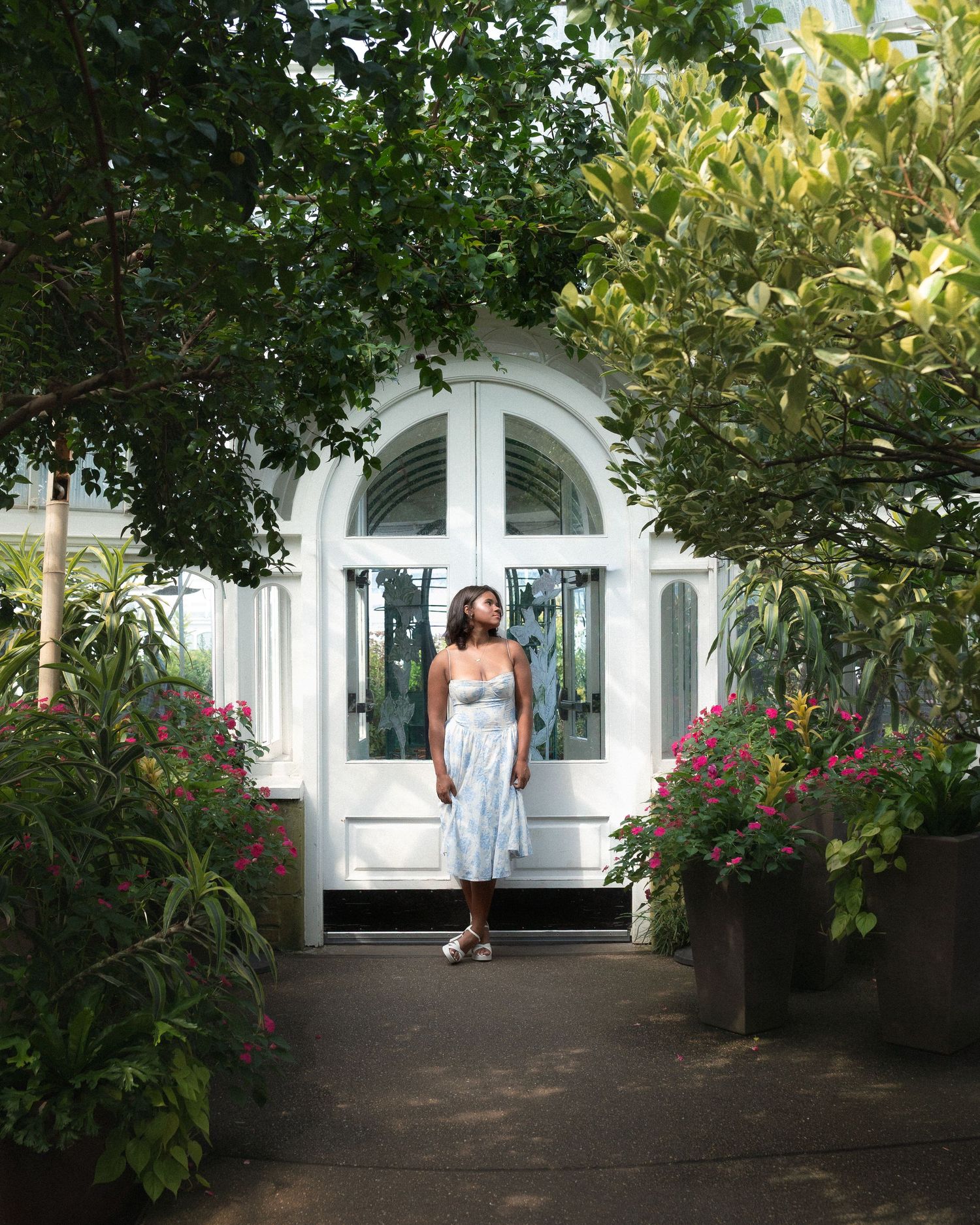 A garden pathway leads to white arched doors with flowering bushes and greenery lining both sides.