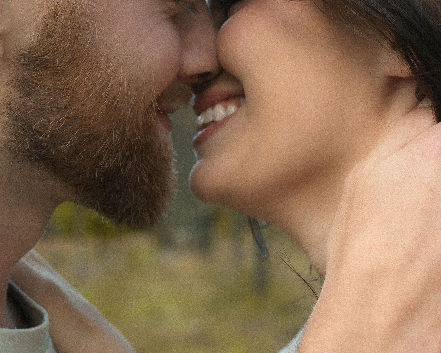 Close-up view of a couple sharing an intimate kiss outdoors with soft natural lighting.