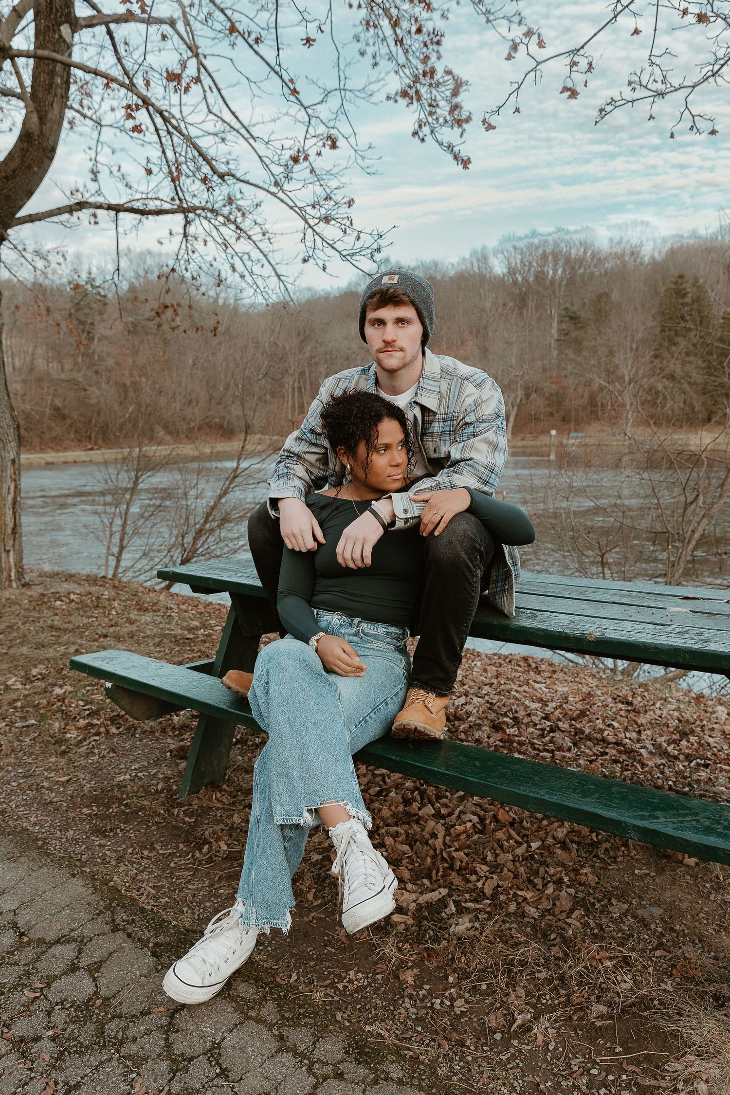 Couple sitting cozy on a green bench by the water, storytelling edit with film warmth and laidback outdoor vibes.