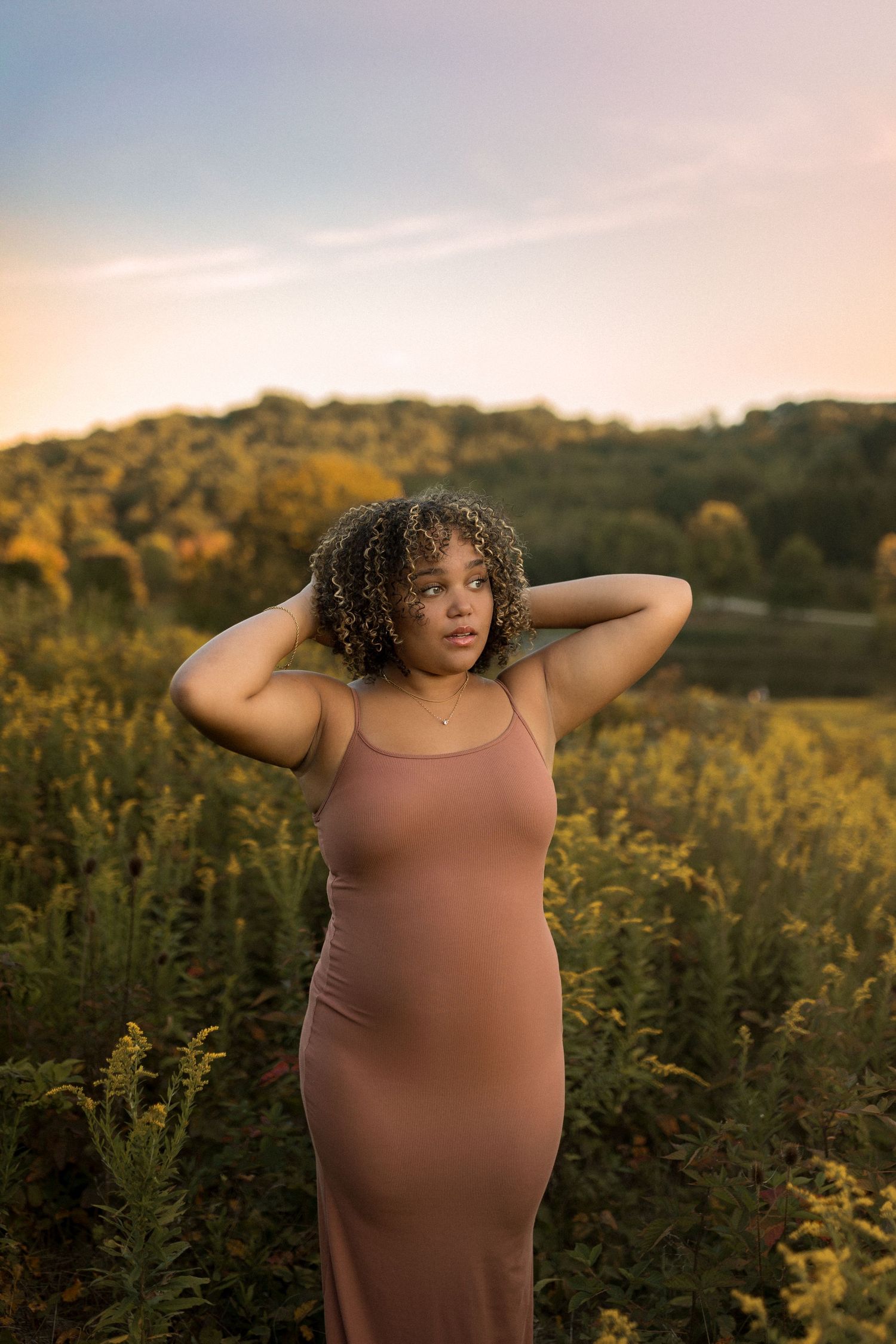 Person in brown dress poses in field of wildflowers during golden hour.