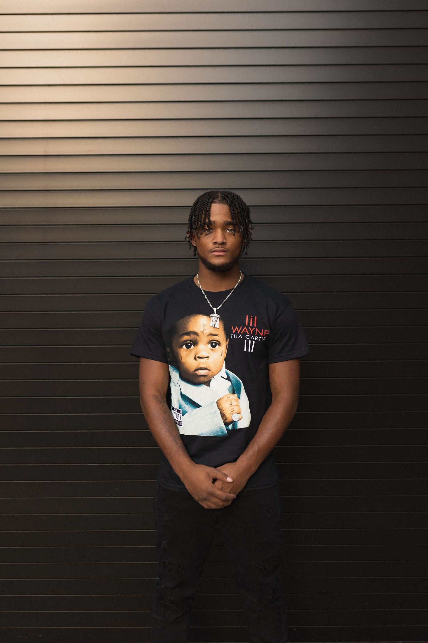 Person wearing t-shirt with graphic print standing against dark striped wall.
