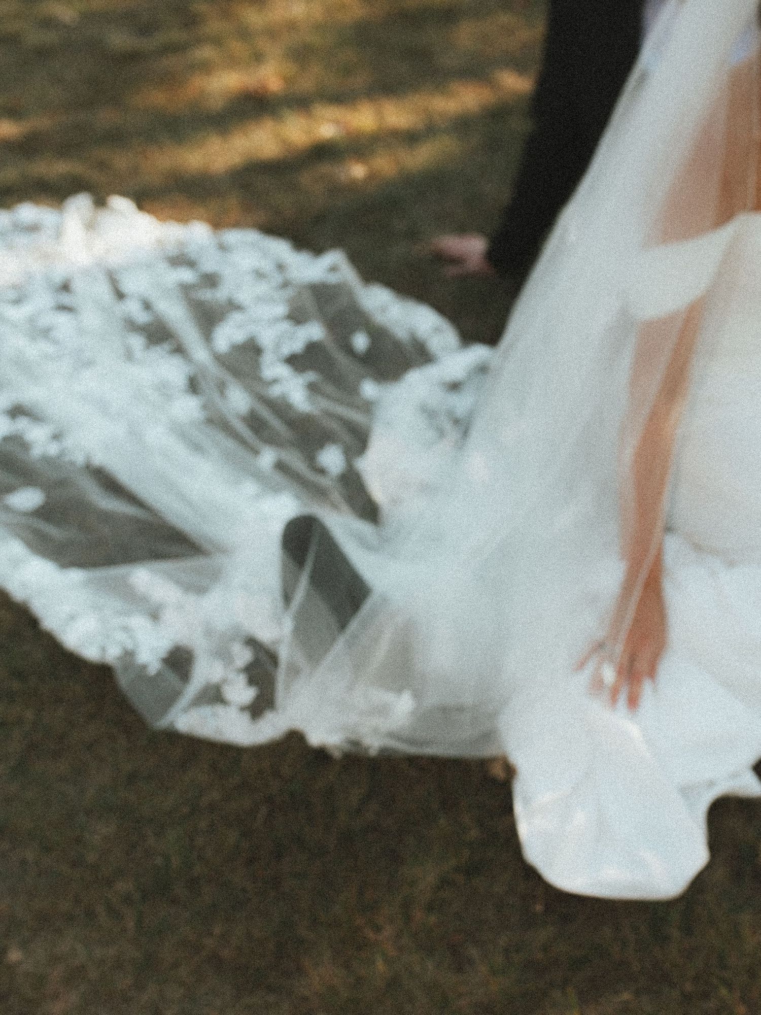 Flowing white wedding dress train with delicate lace details trails elegantly across a dark wooden floor.