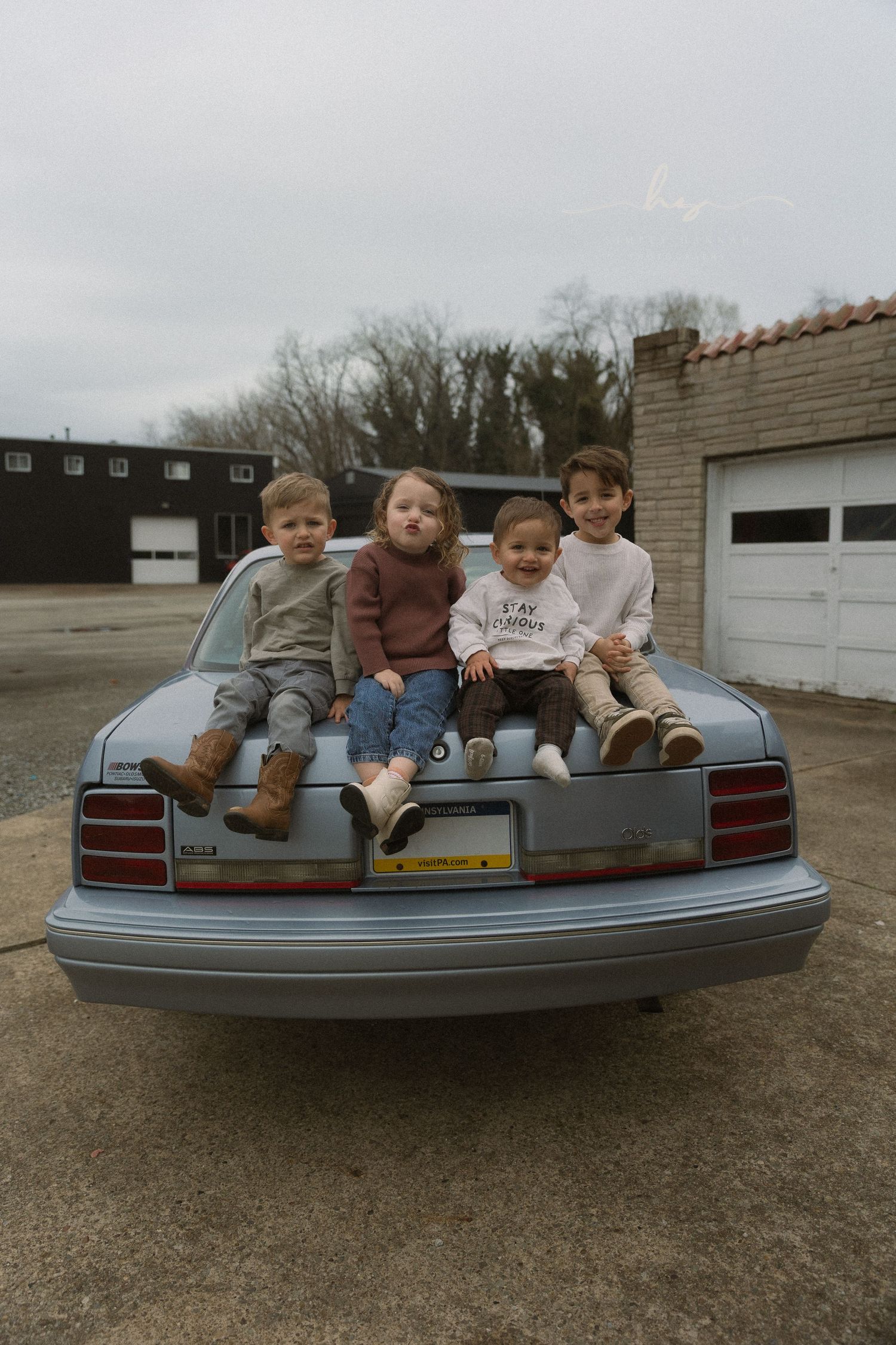 Four young siblings sitting on a classic car trunk, lifestyle family photography with retro vibes and real smiles.