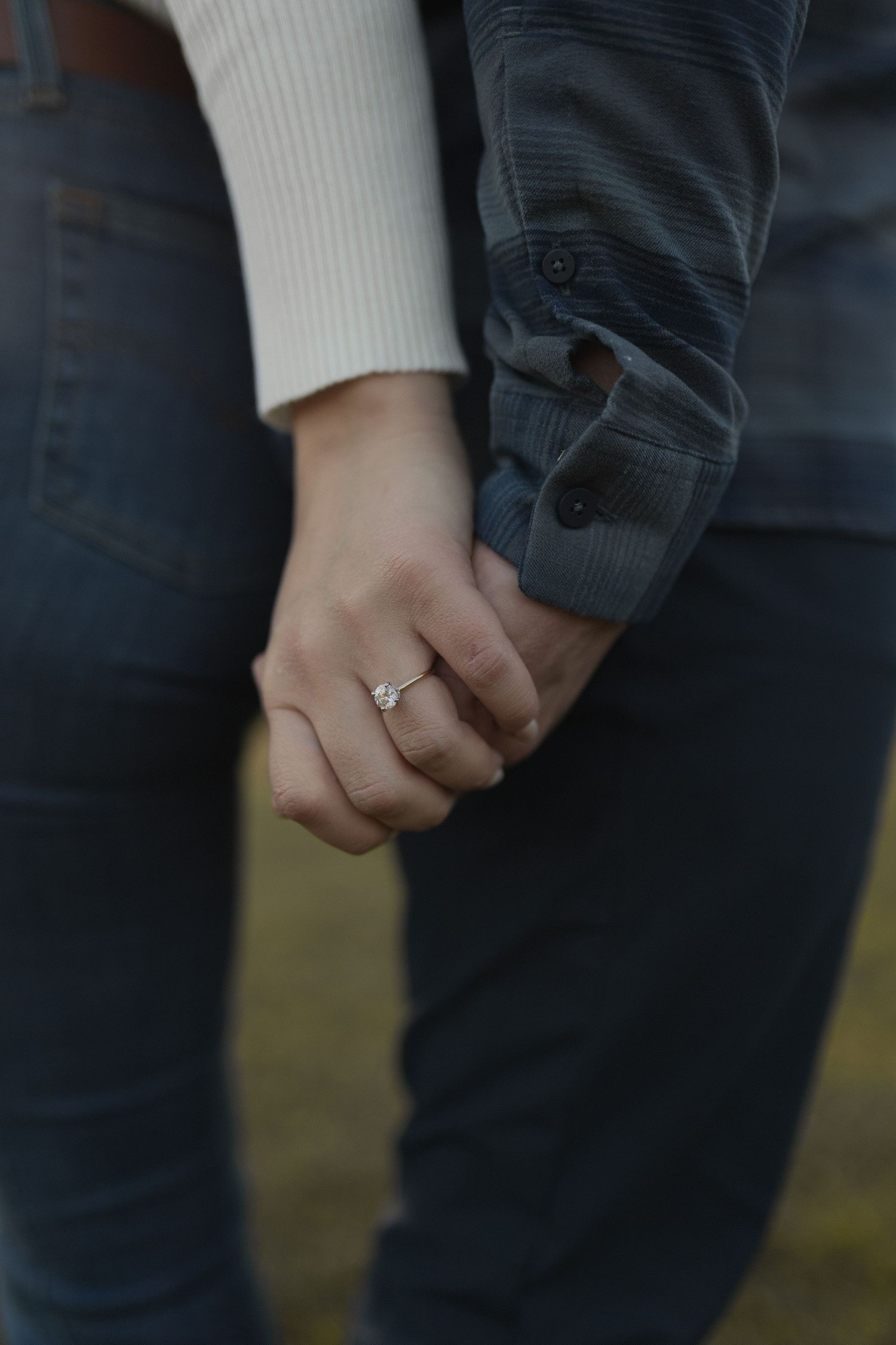 Close-up of intertwined hands with an engagement ring in casual attire.