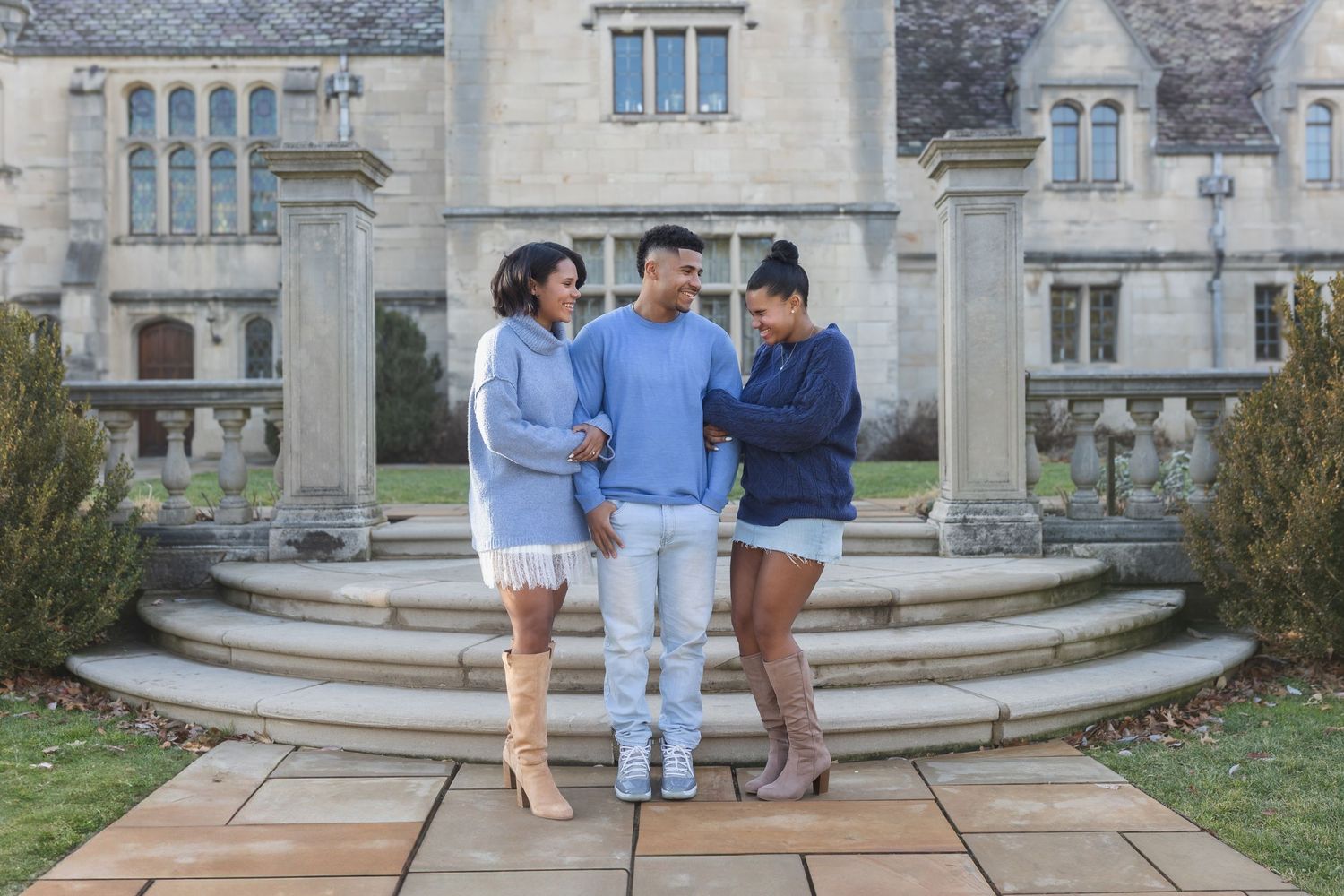 Three people posing on stone steps outside a grand historic building.