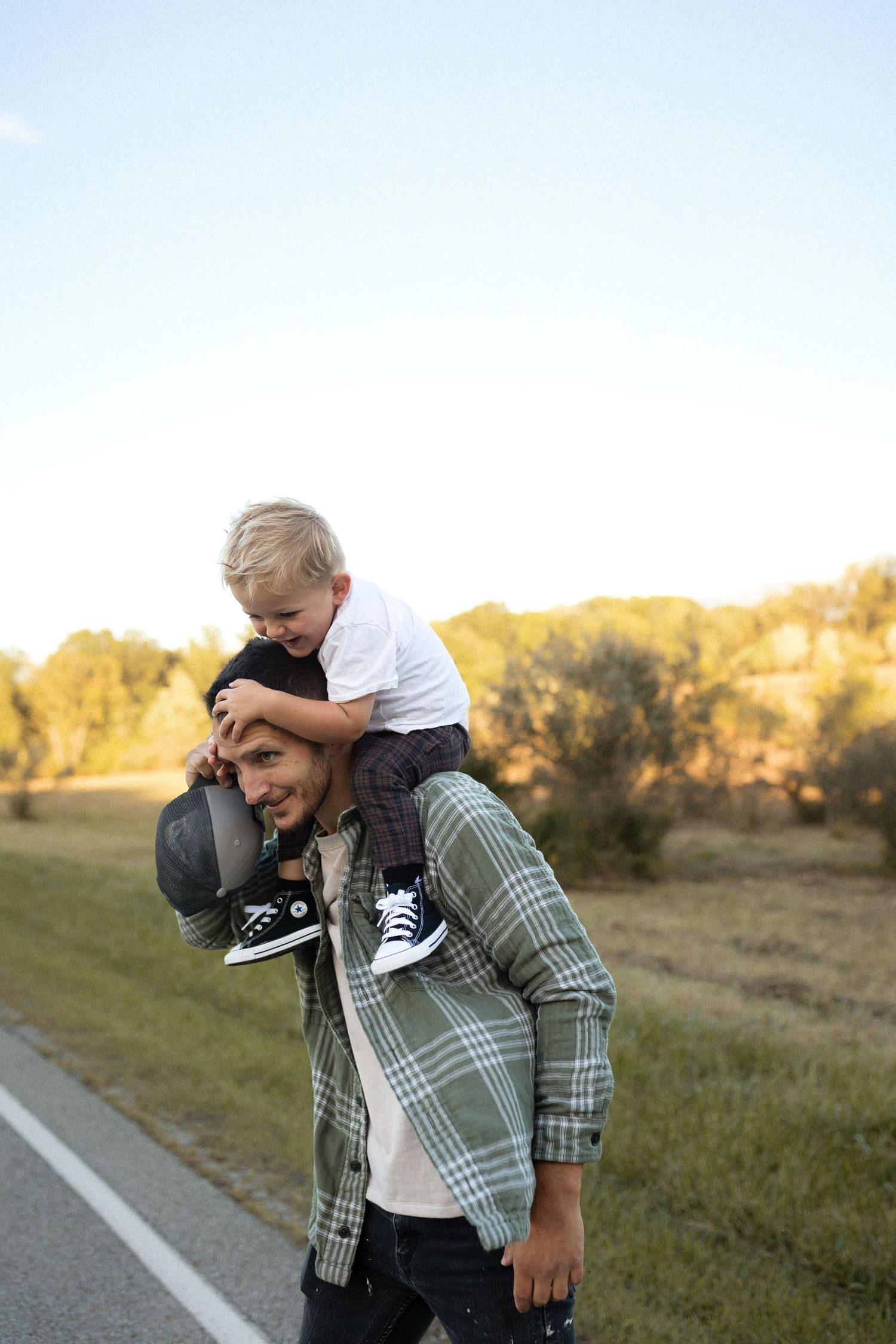 Child riding on shoulders while wearing casual outdoor clothing on a rural road.