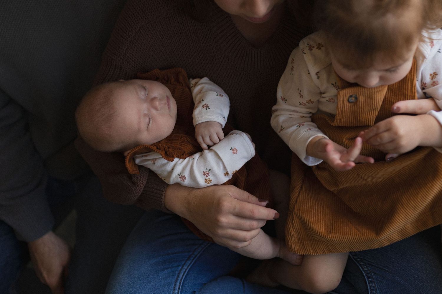 A sleeping infant rests peacefully while being held in brown and white clothing.