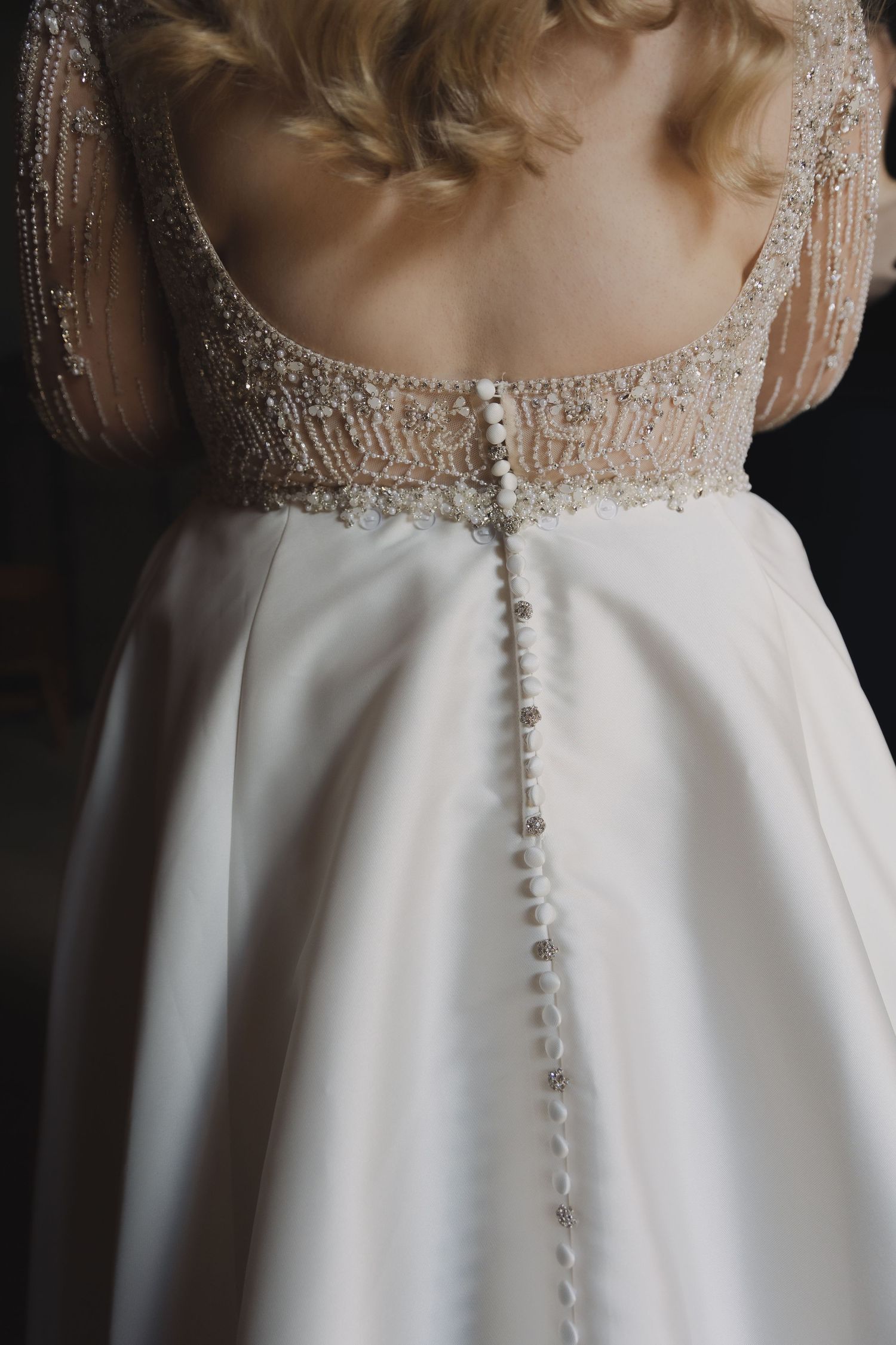 Close up detail of pearl buttons and beaded lace on back of white wedding dress.