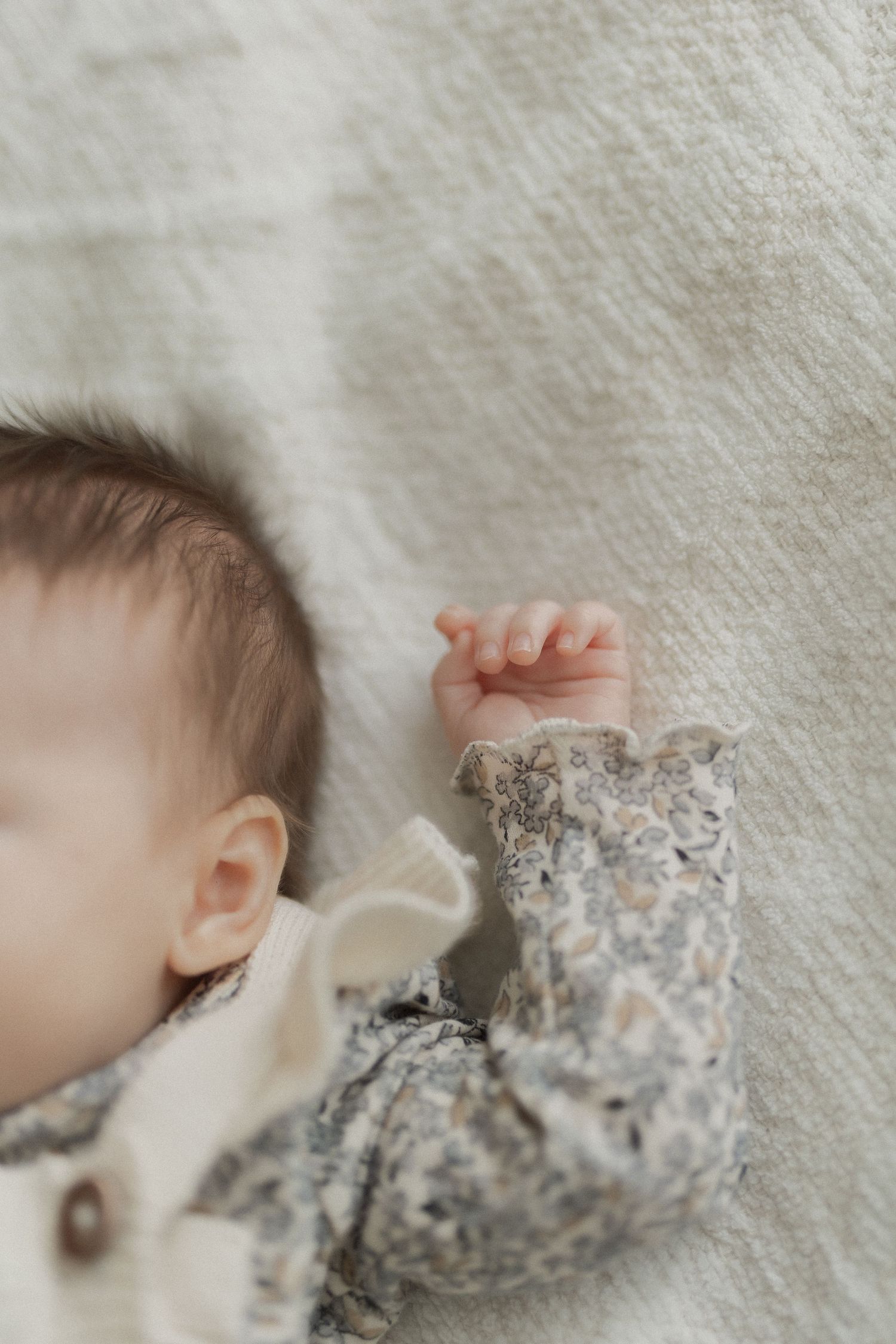 Sleeping baby in floral clothing against white textured fabric.