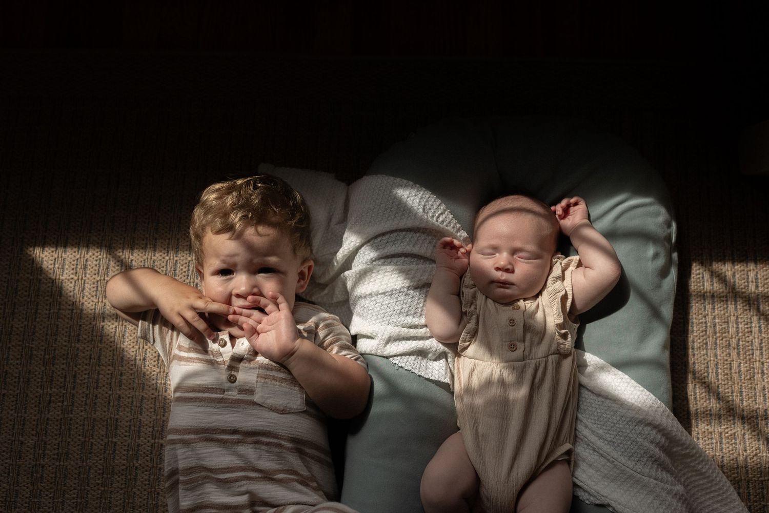 Two infants lying together on a white surface with dramatic shadows and lighting.