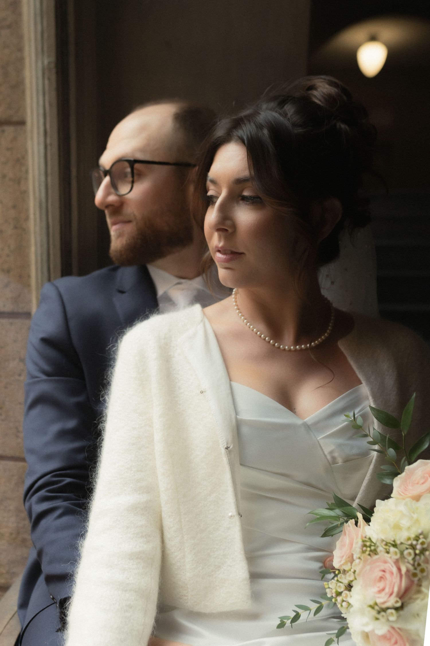 Elegant couple in wedding attire looking out a window together.