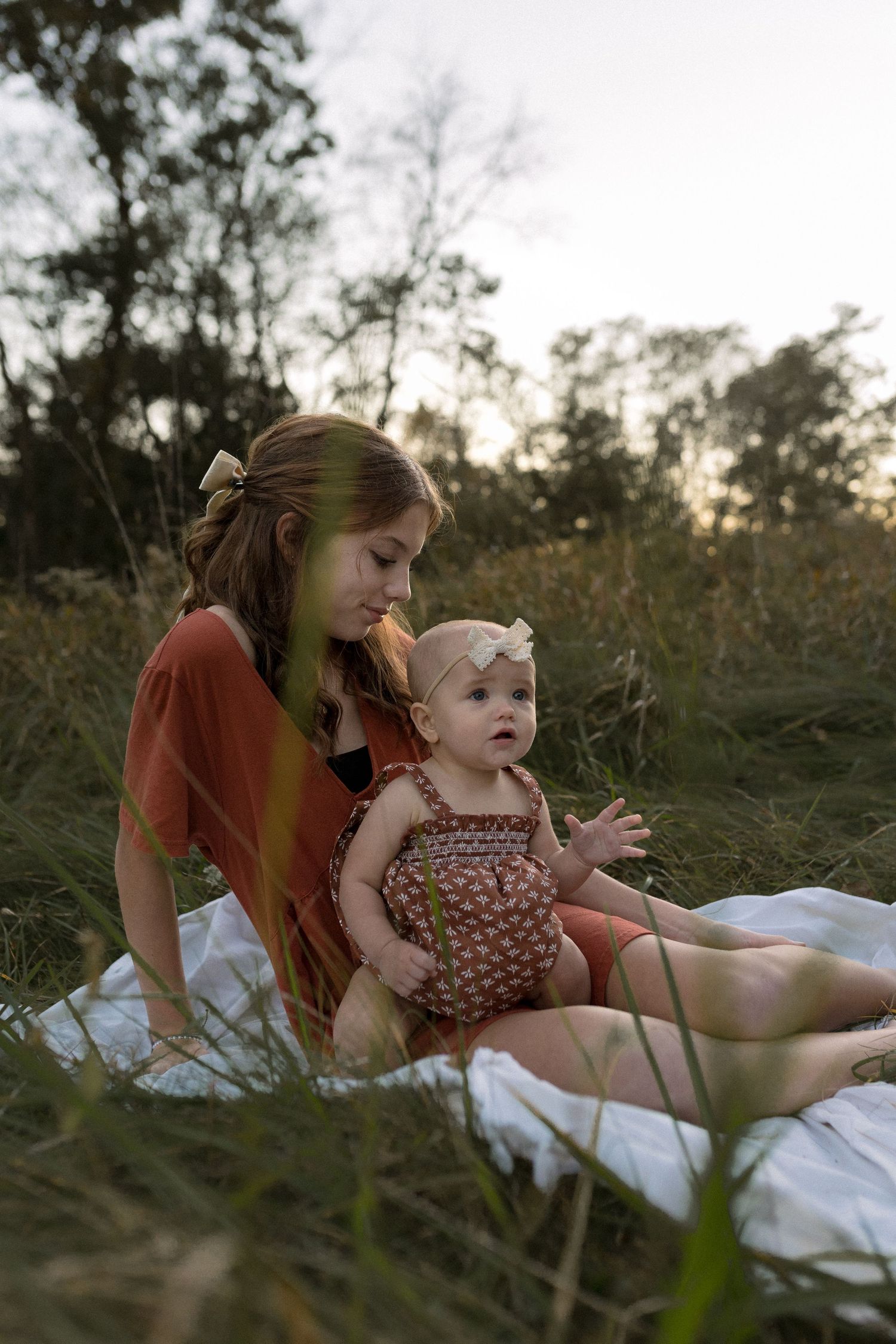 A peaceful outdoor portrait on a white blanket amidst tall grass at golden hour.
