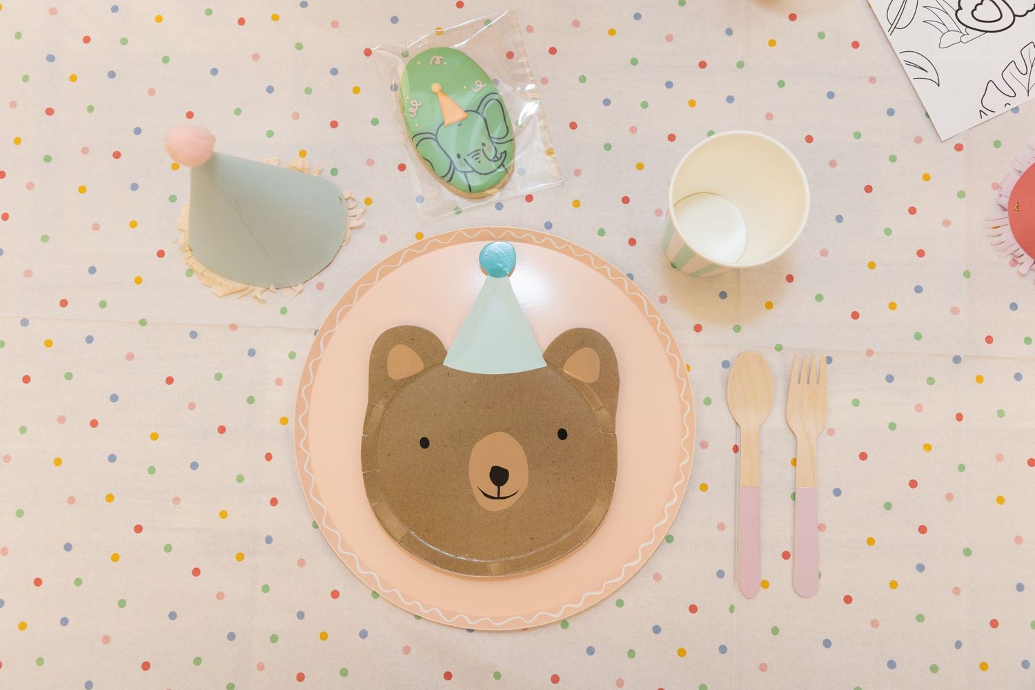 A cute bear-themed party place setting with pastel utensils on a polka dot tablecloth.