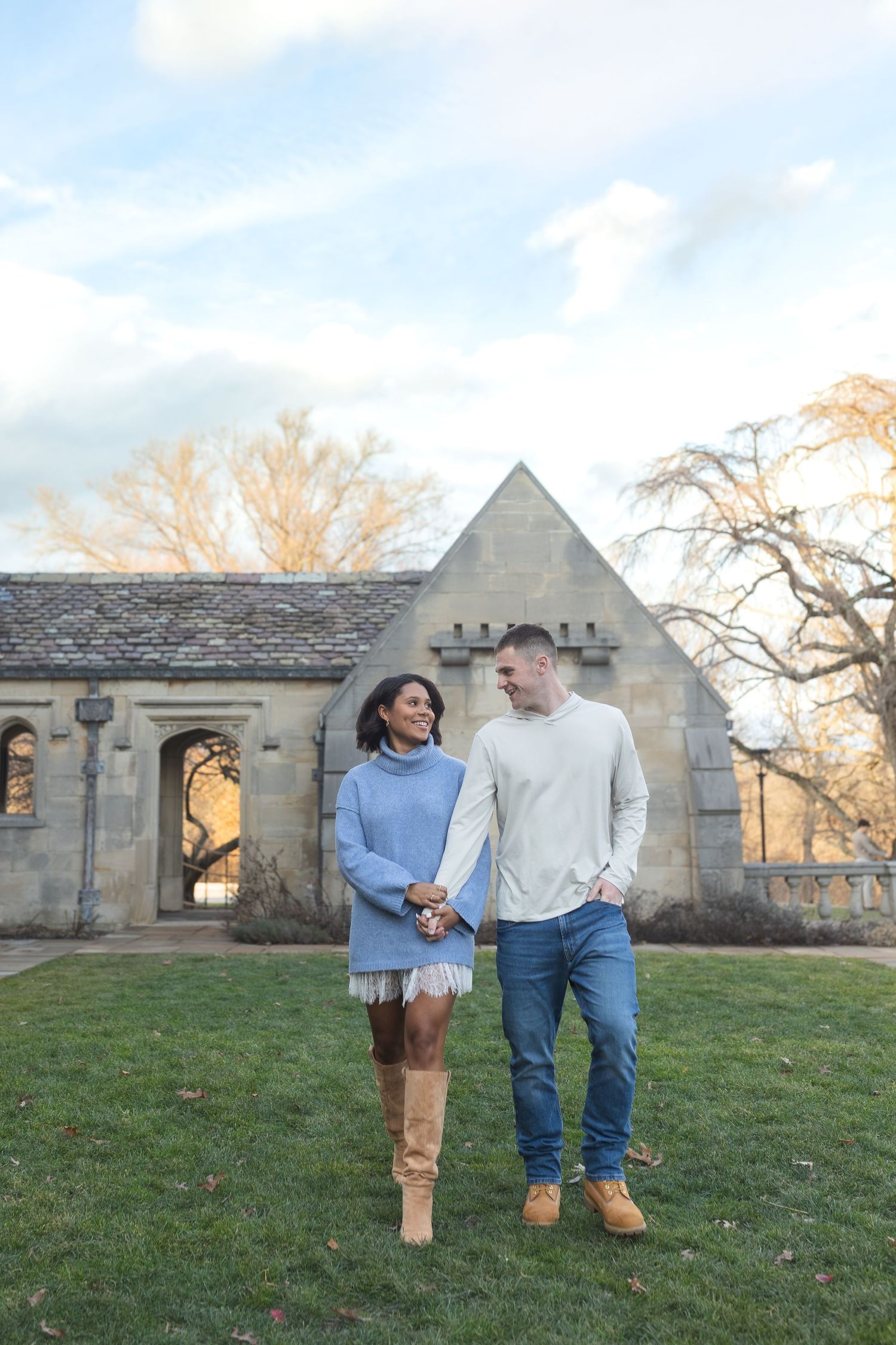 A couple walking together on grass in front of Gothic architecture during golden hour.