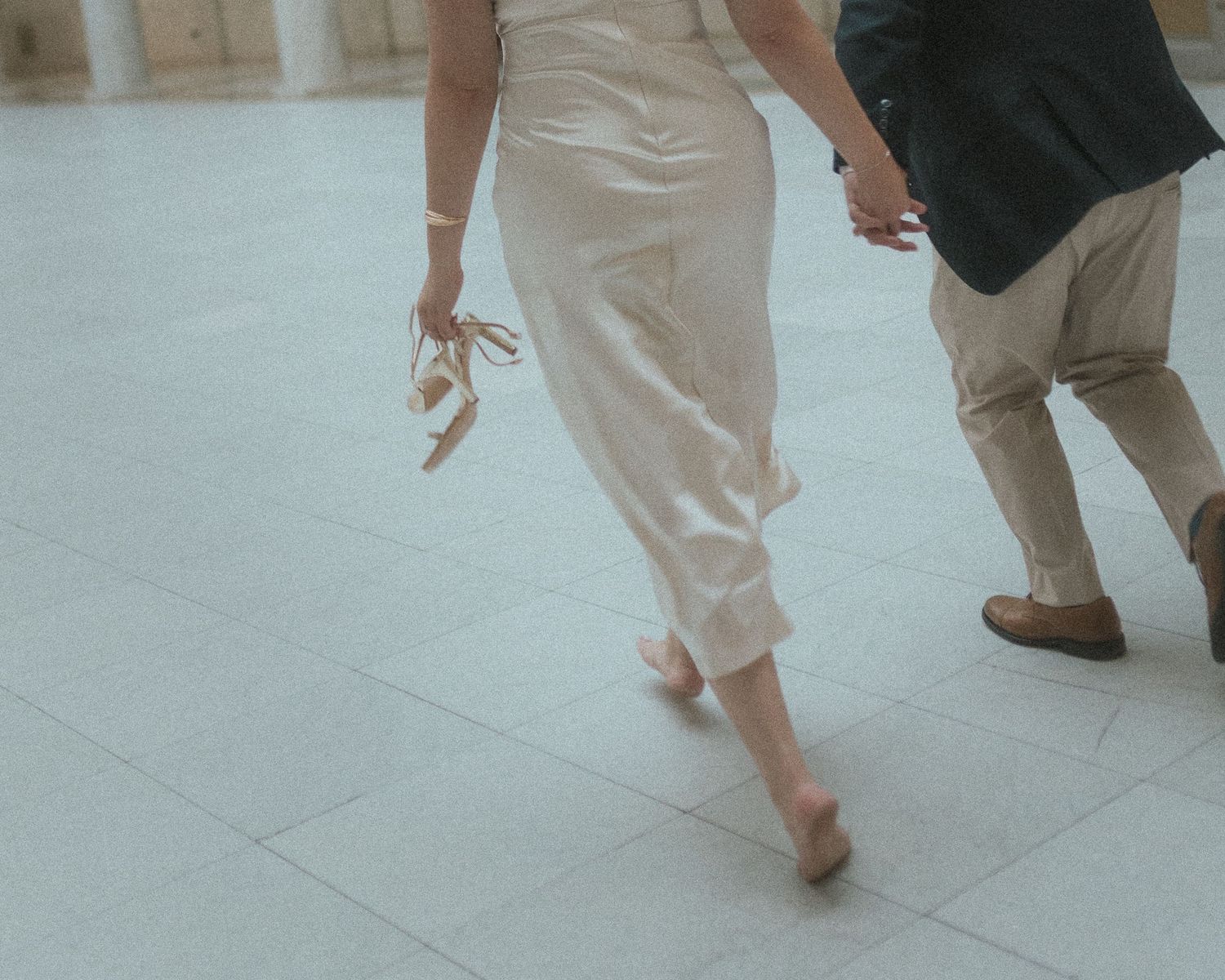 Feet of dancers in white clothing moving gracefully across a light-colored floor in a dance studio.