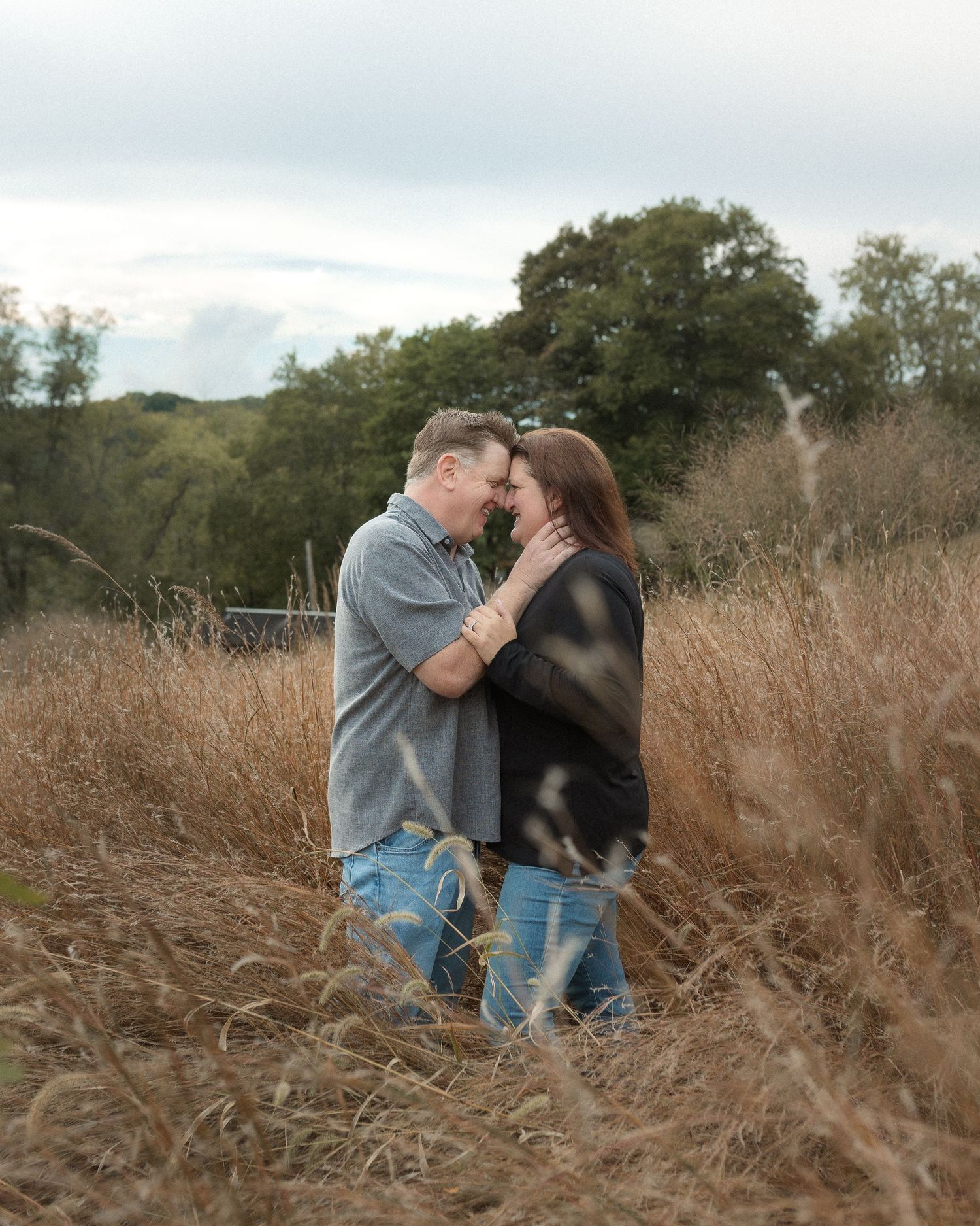 A loving couple shares tender moments while sitting among dried grass in a natural outdoor setting.