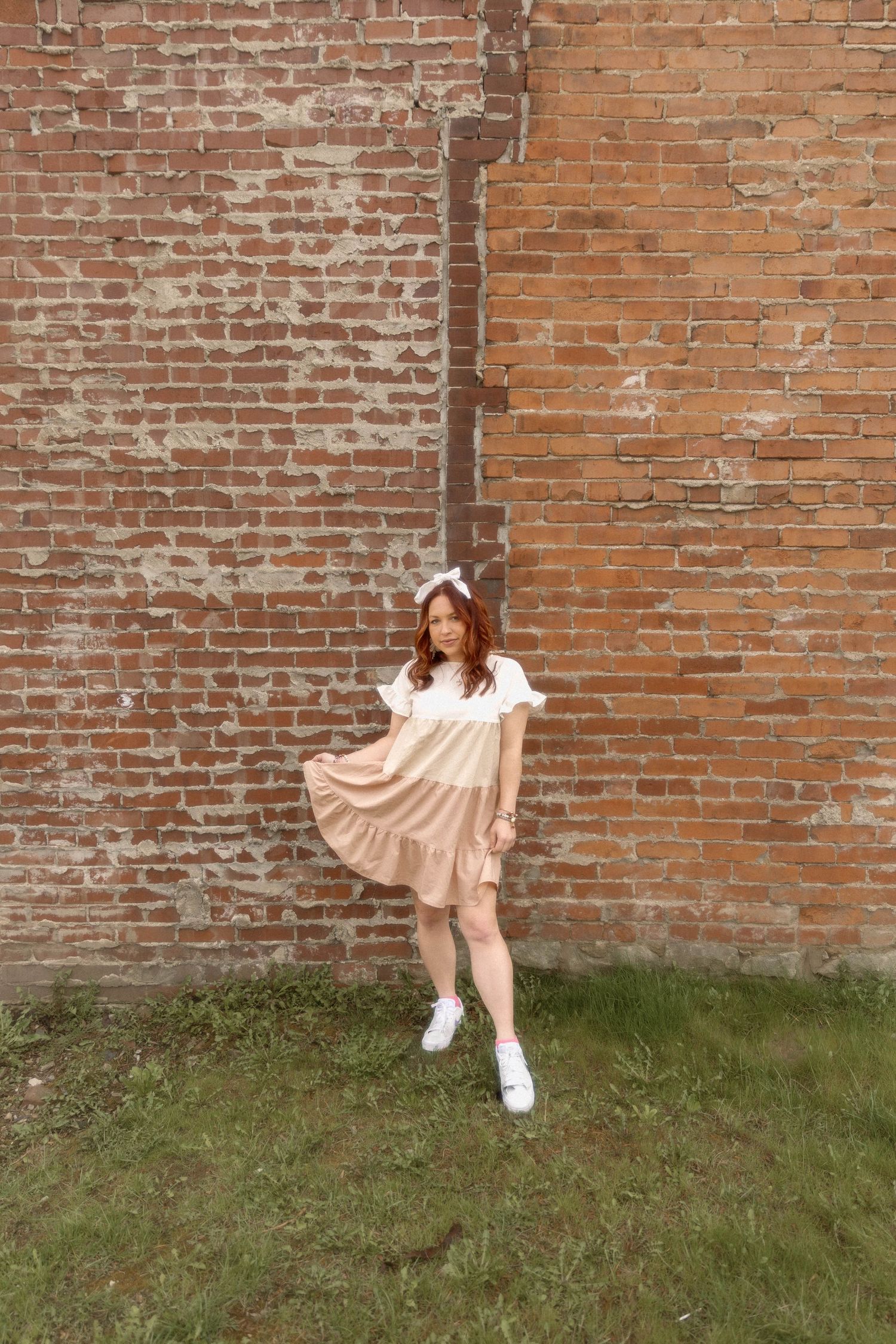 Twirling motion in peach tiered dress against rustic brick wall background.