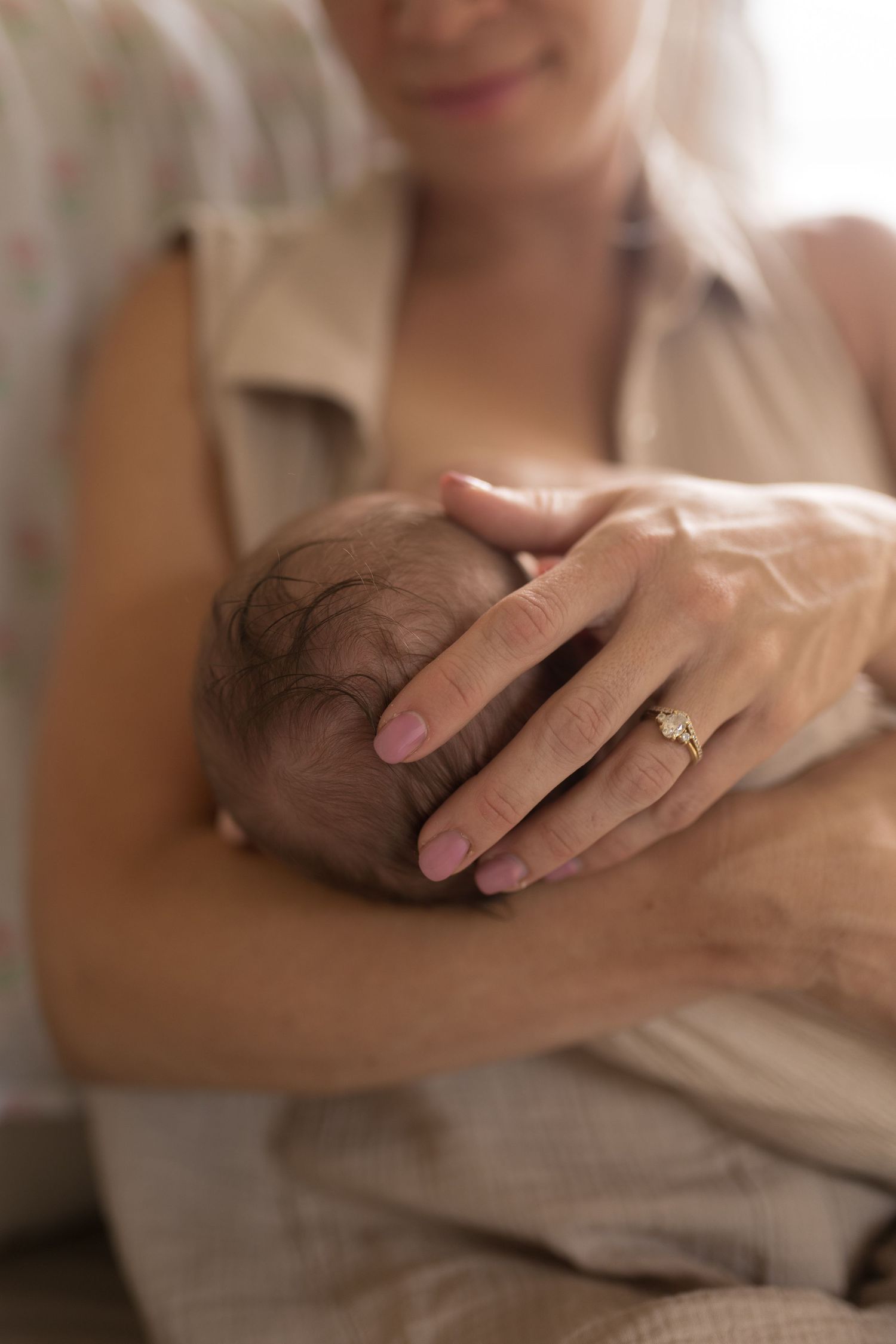 Gentle hand cradling baby's head with engagement ring visible.