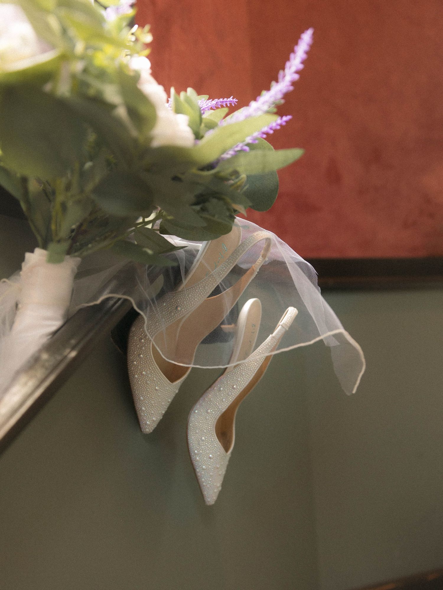 Close-up detail of hanging white decorative elements with metallic accents and delicate foliage against a textured backdrop.