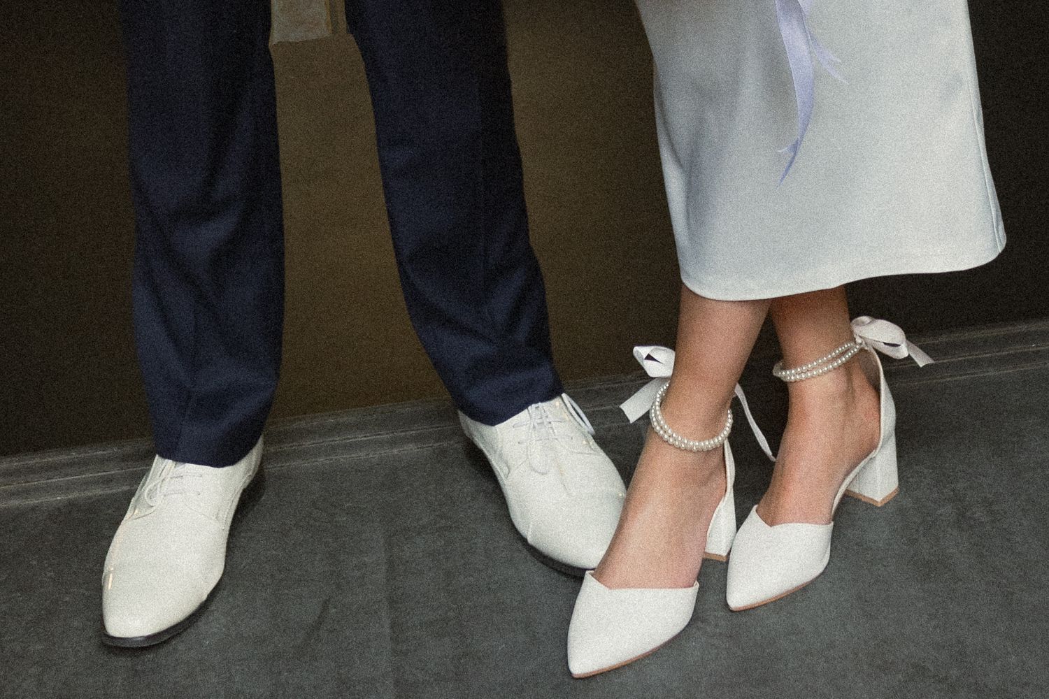 A close-up of elegant white wedding shoes alongside formal dress shoes.