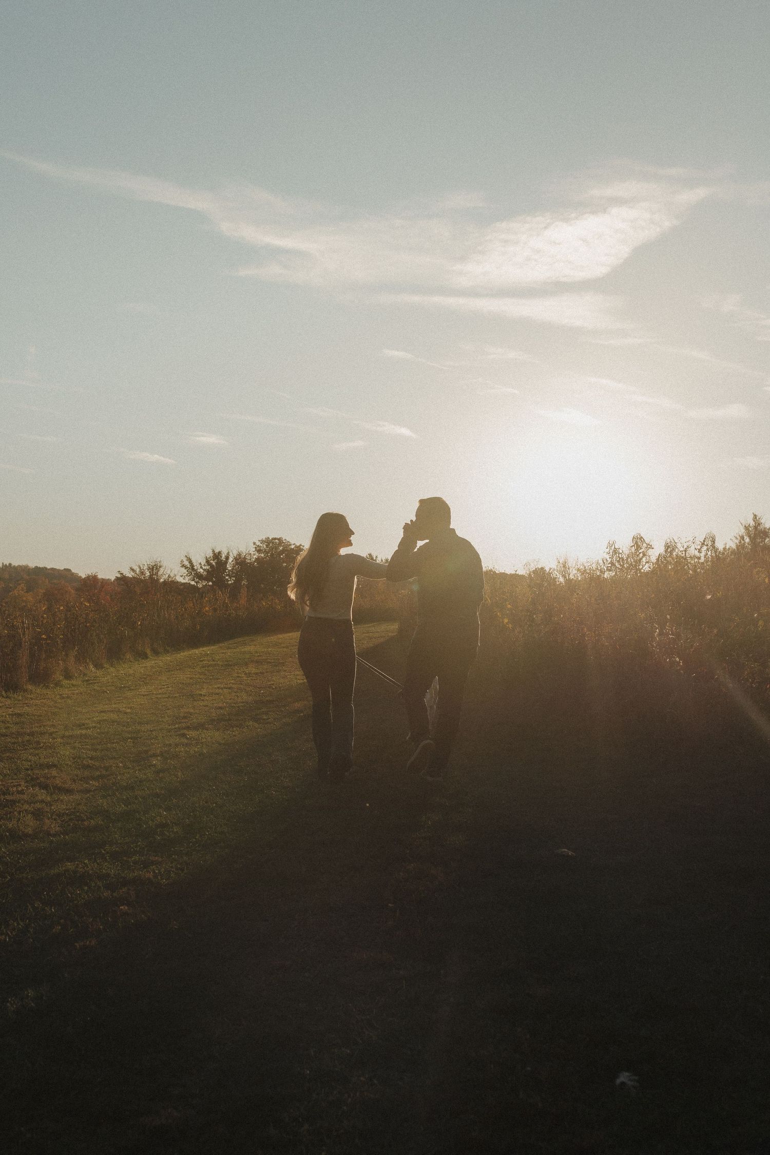 Silhouette of couple walking together at sunset on a hilltop path.
