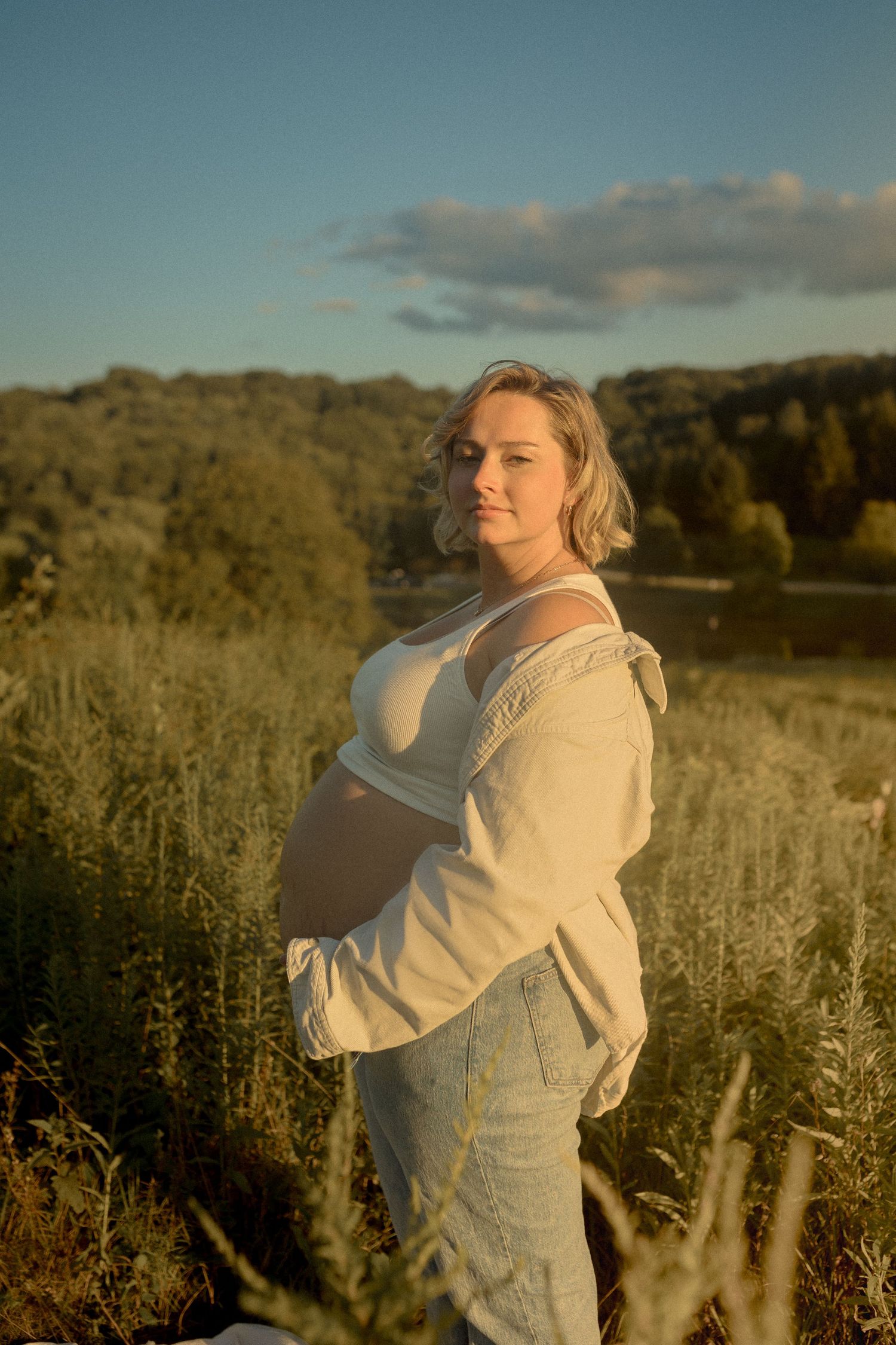 Person in white top and jeans poses in wildflower field during sunset.