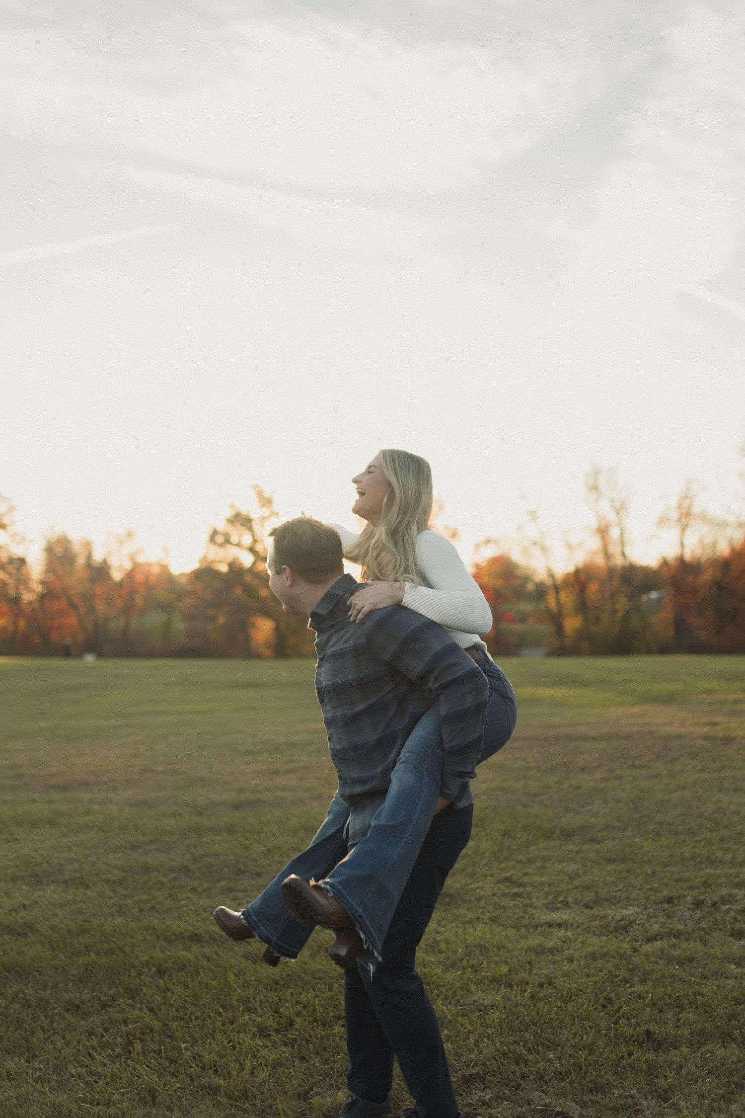 A playful couple enjoying a piggyback ride in an autumn field at dusk.