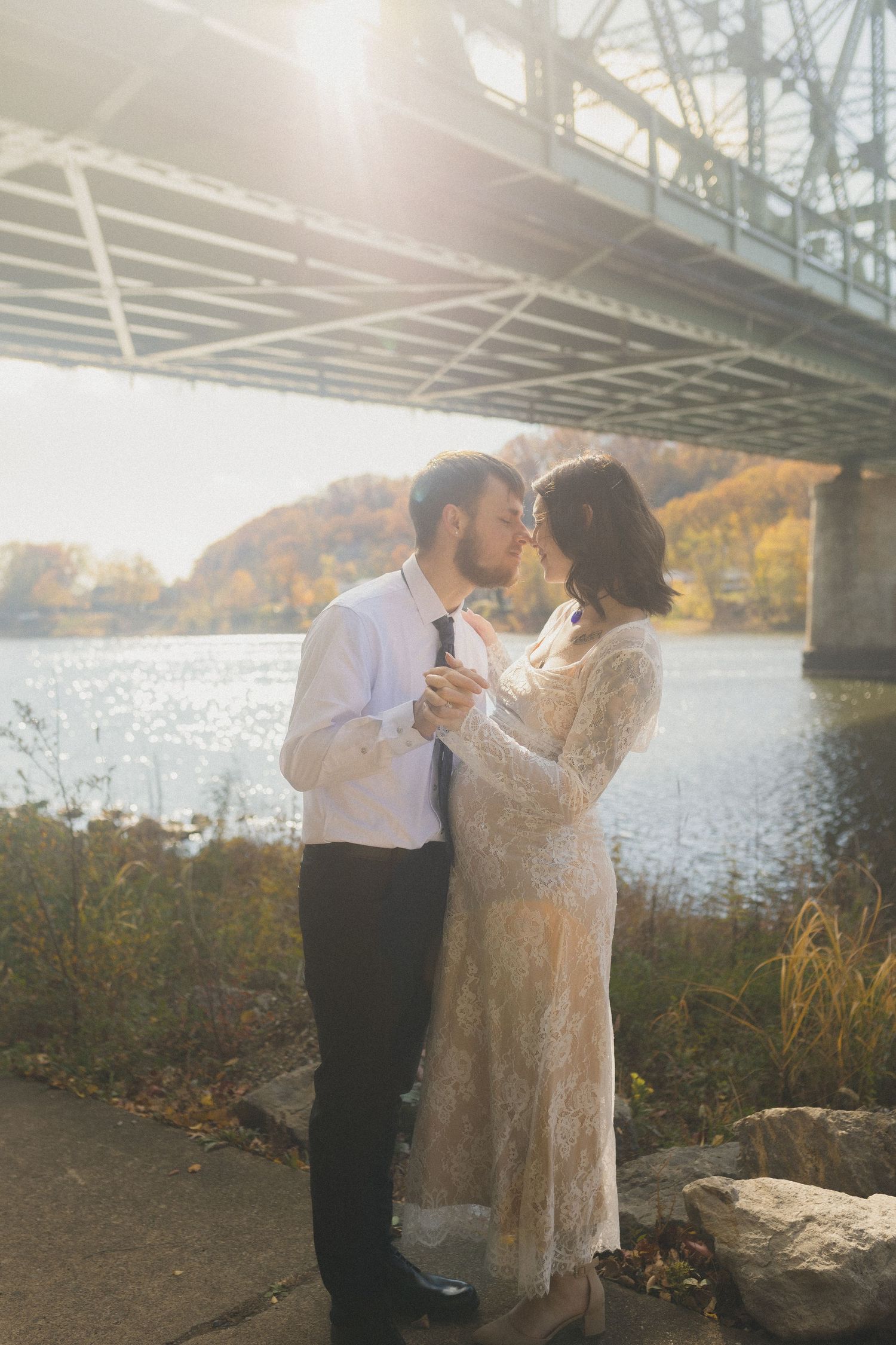 Romantic autumn wedding photo under bridge by river.