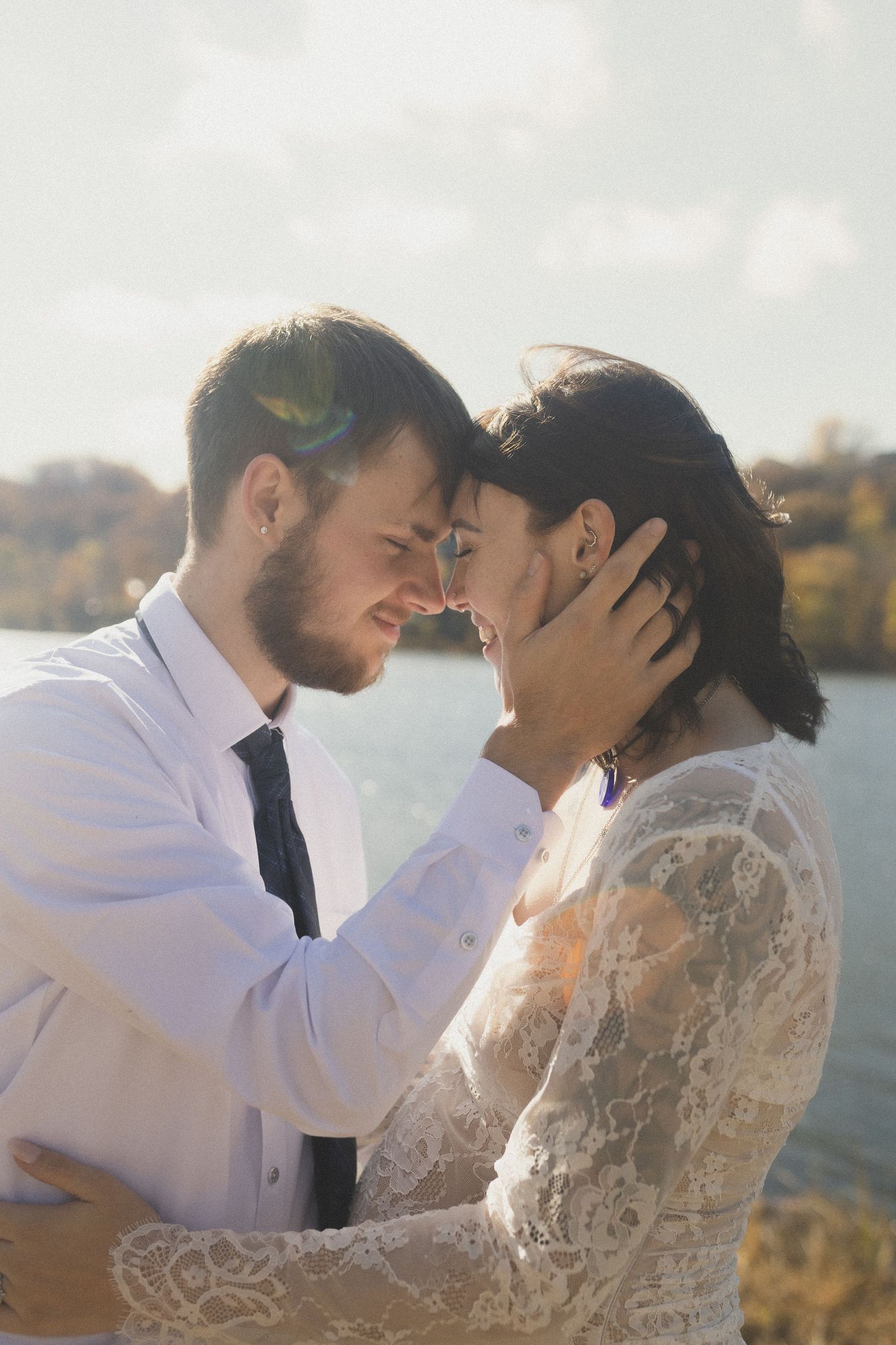 A romantic moment between a couple in wedding attire sharing an intimate embrace by a lake at sunset.