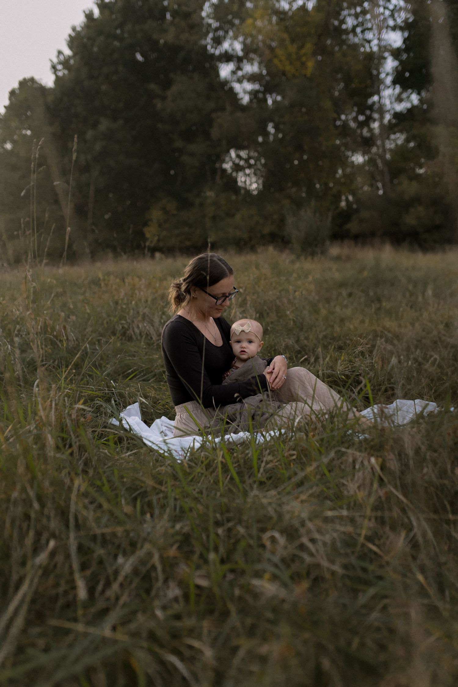 A sweet outdoor moment on a blanket in a grassy field at sunset.