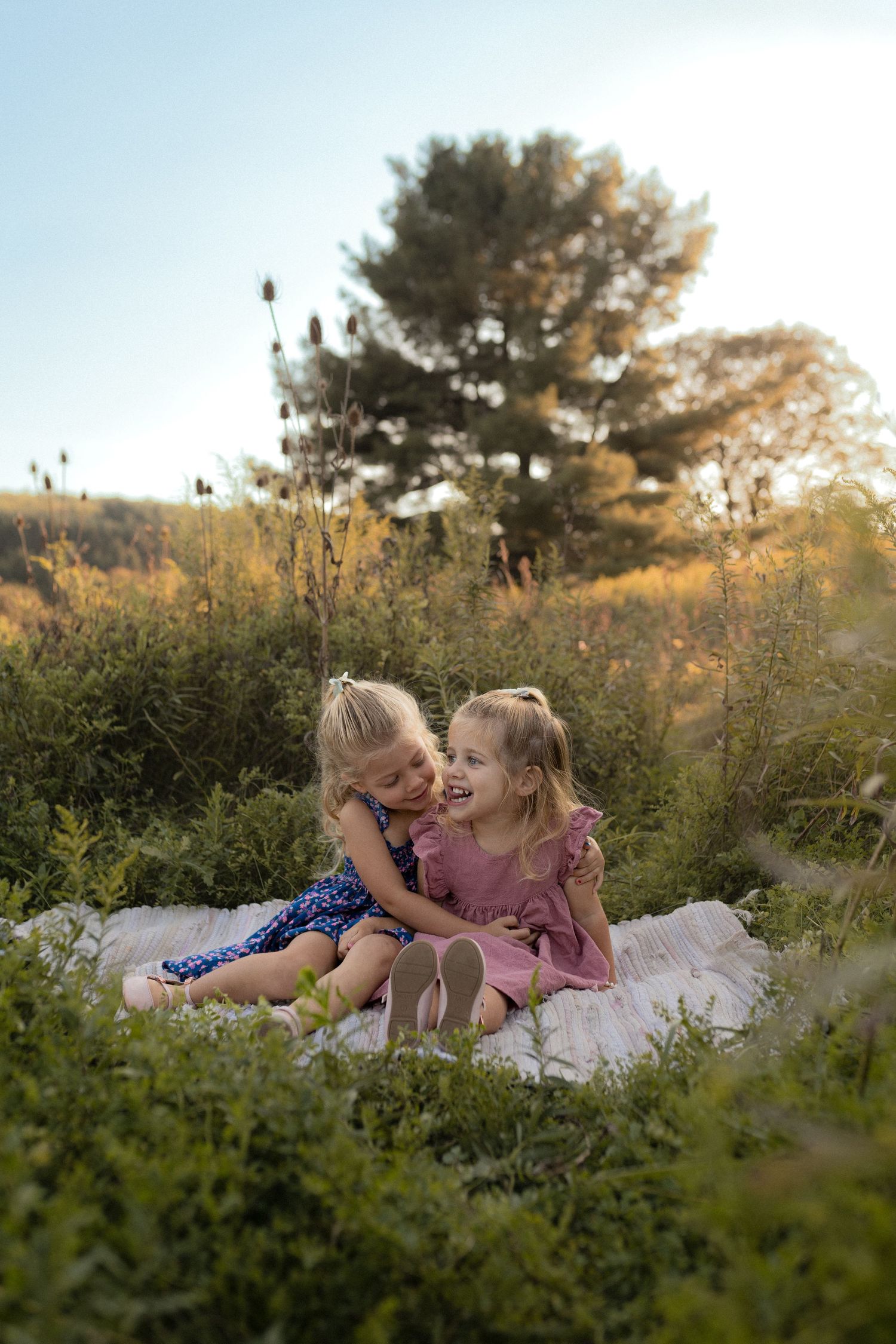 Two children sharing a joyful moment on a blanket in a sunlit field.
