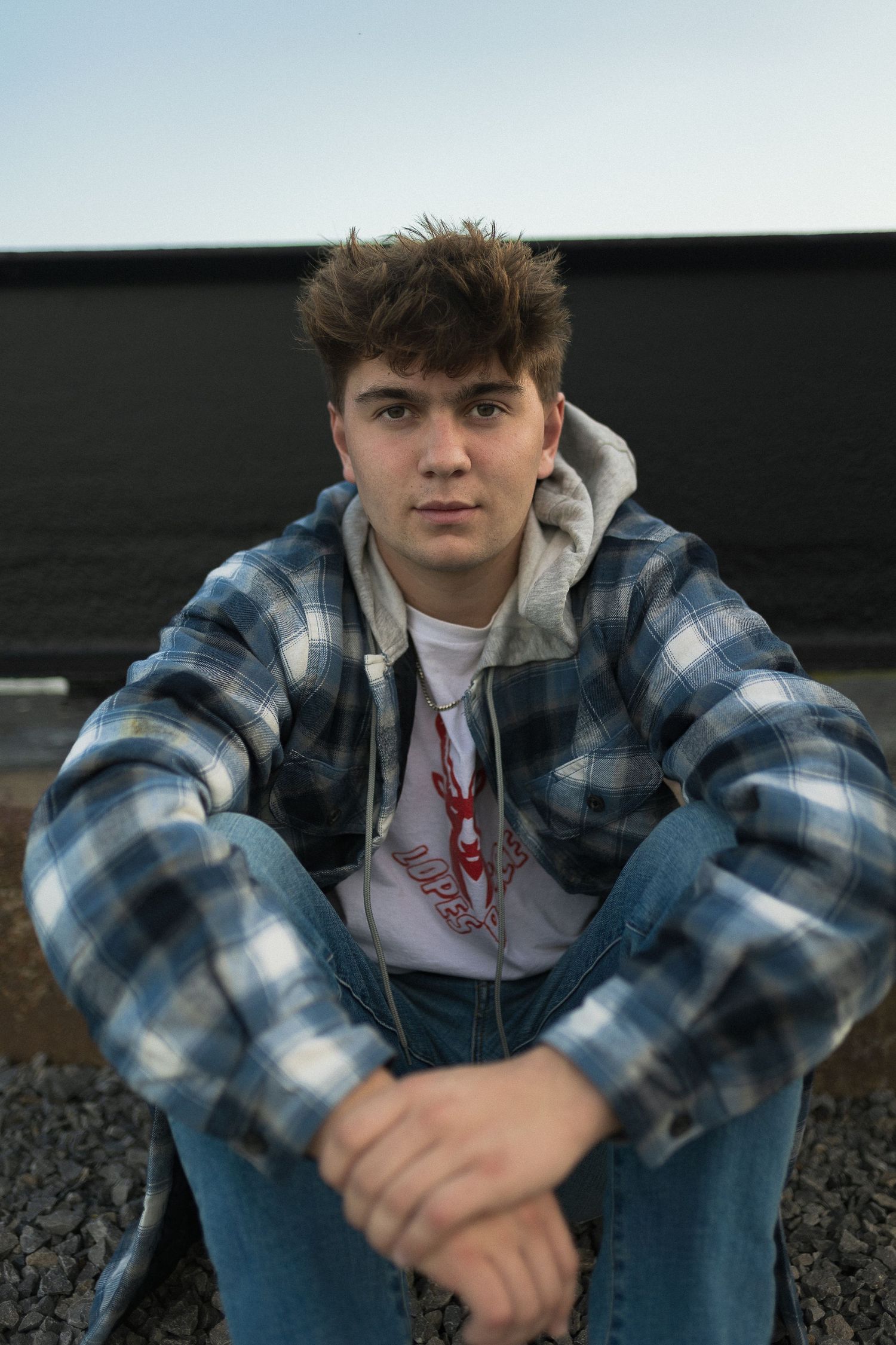 Person in plaid jacket and hoodie sitting outdoors during golden hour.