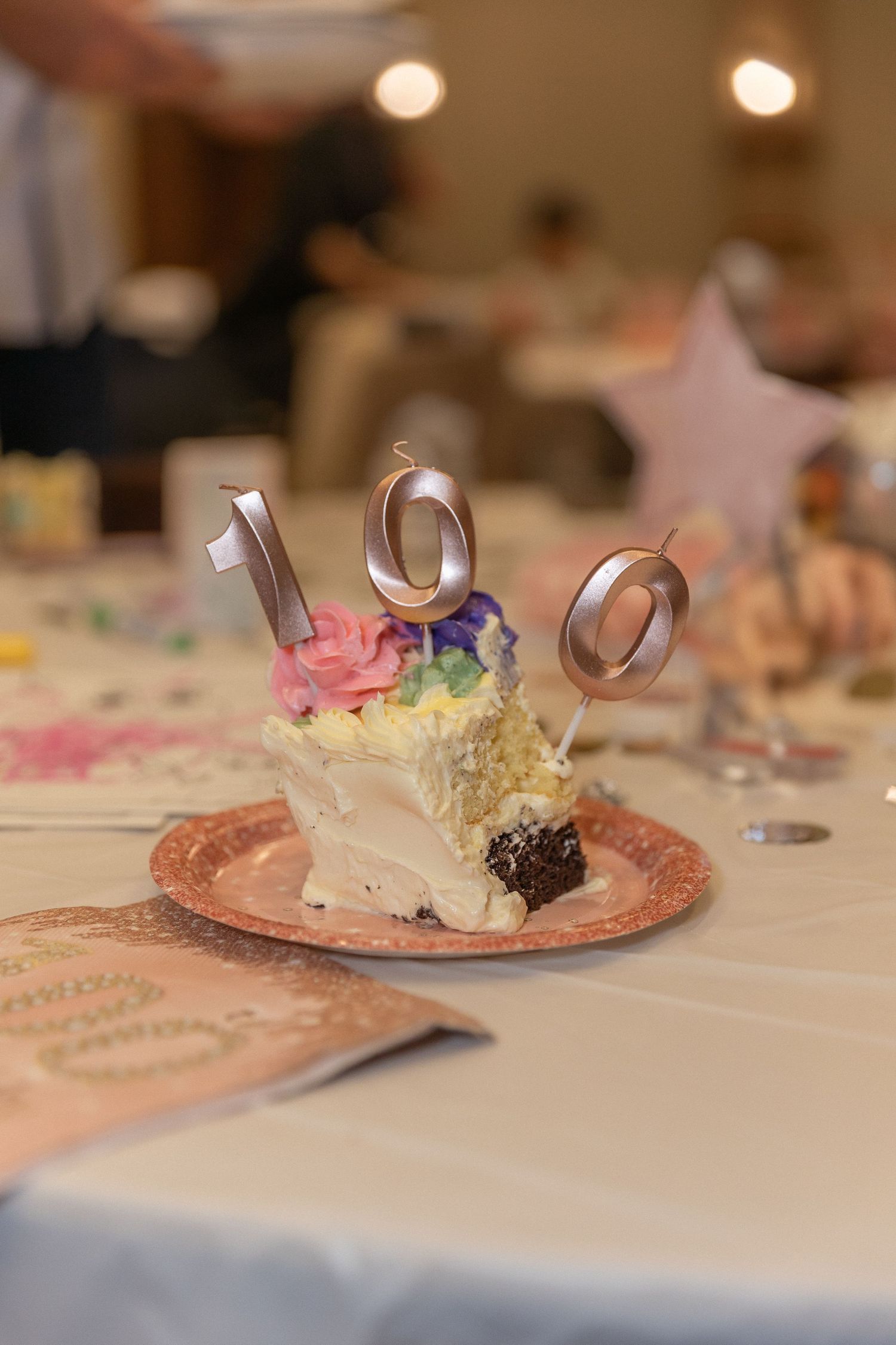 A decorated cake with metallic number candles 100 on a pink plate.