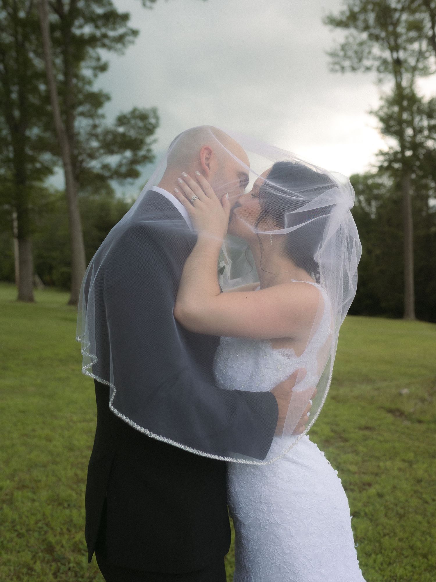A couple shares an intimate kiss under a delicate veil in an outdoor garden setting.